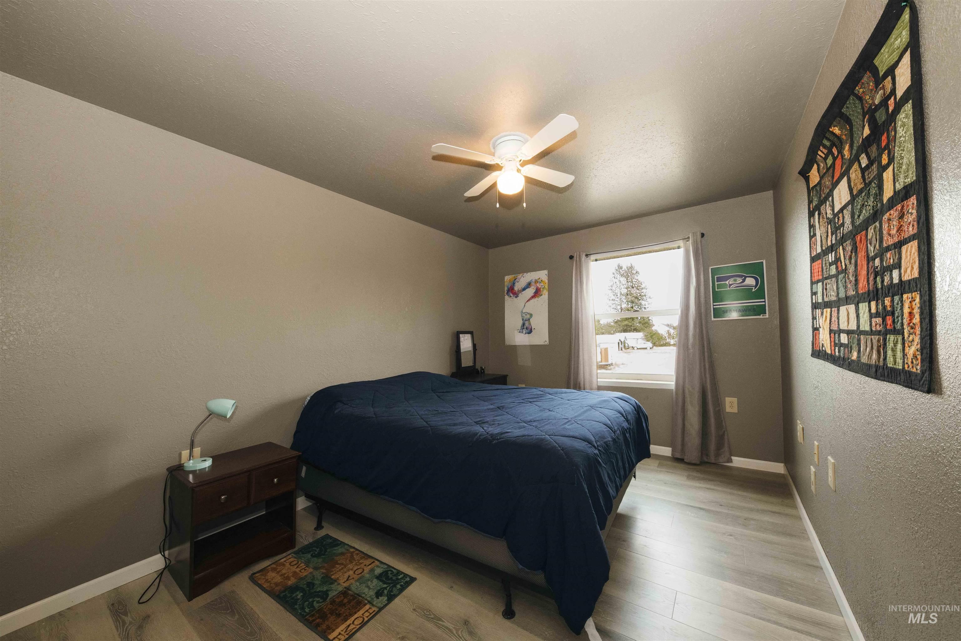 Bedroom featuring a textured wall, light wood-style flooring, and a ceiling fan
