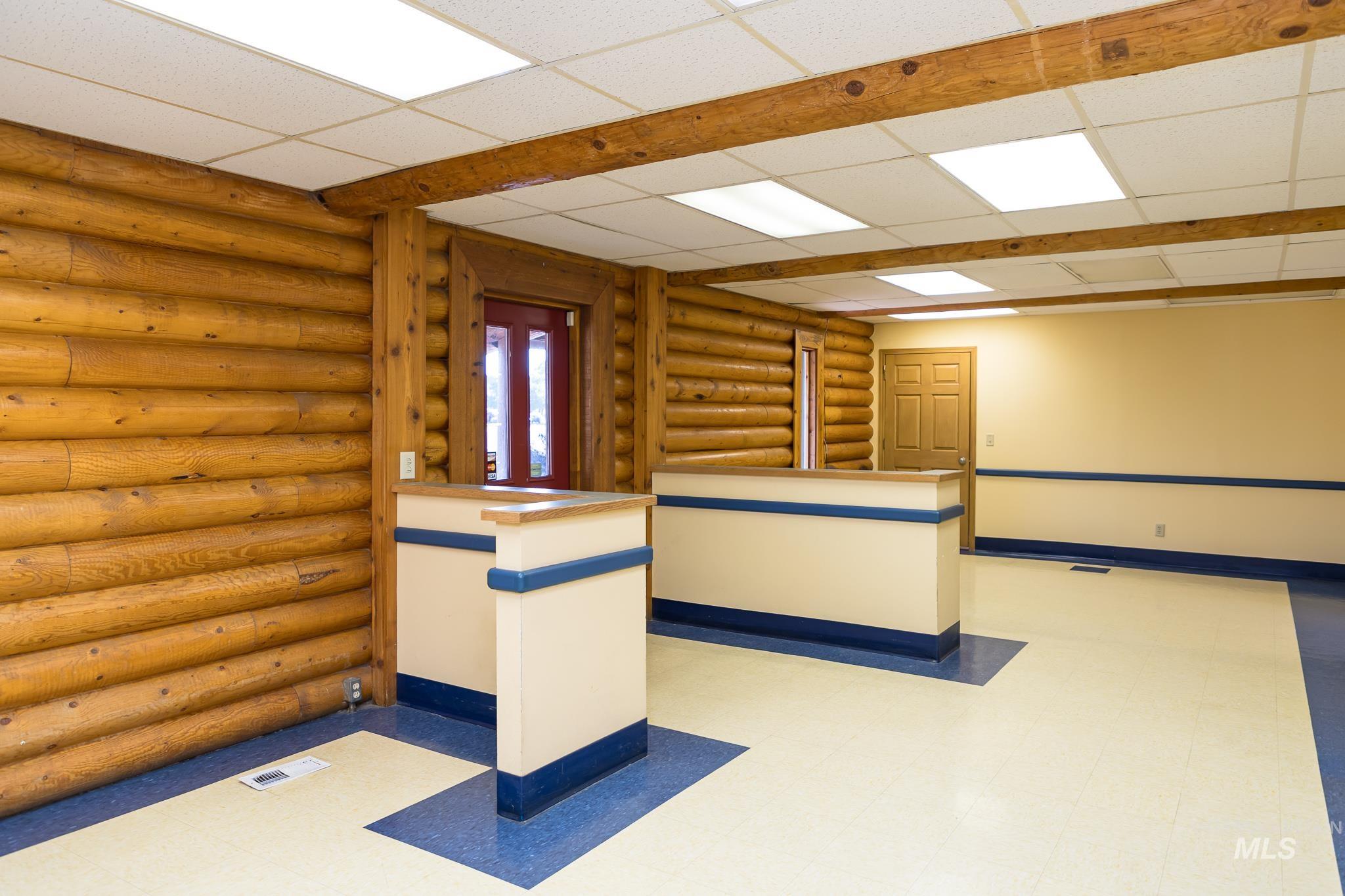 Empty room featuring light flooring, log walls, and a drop ceiling