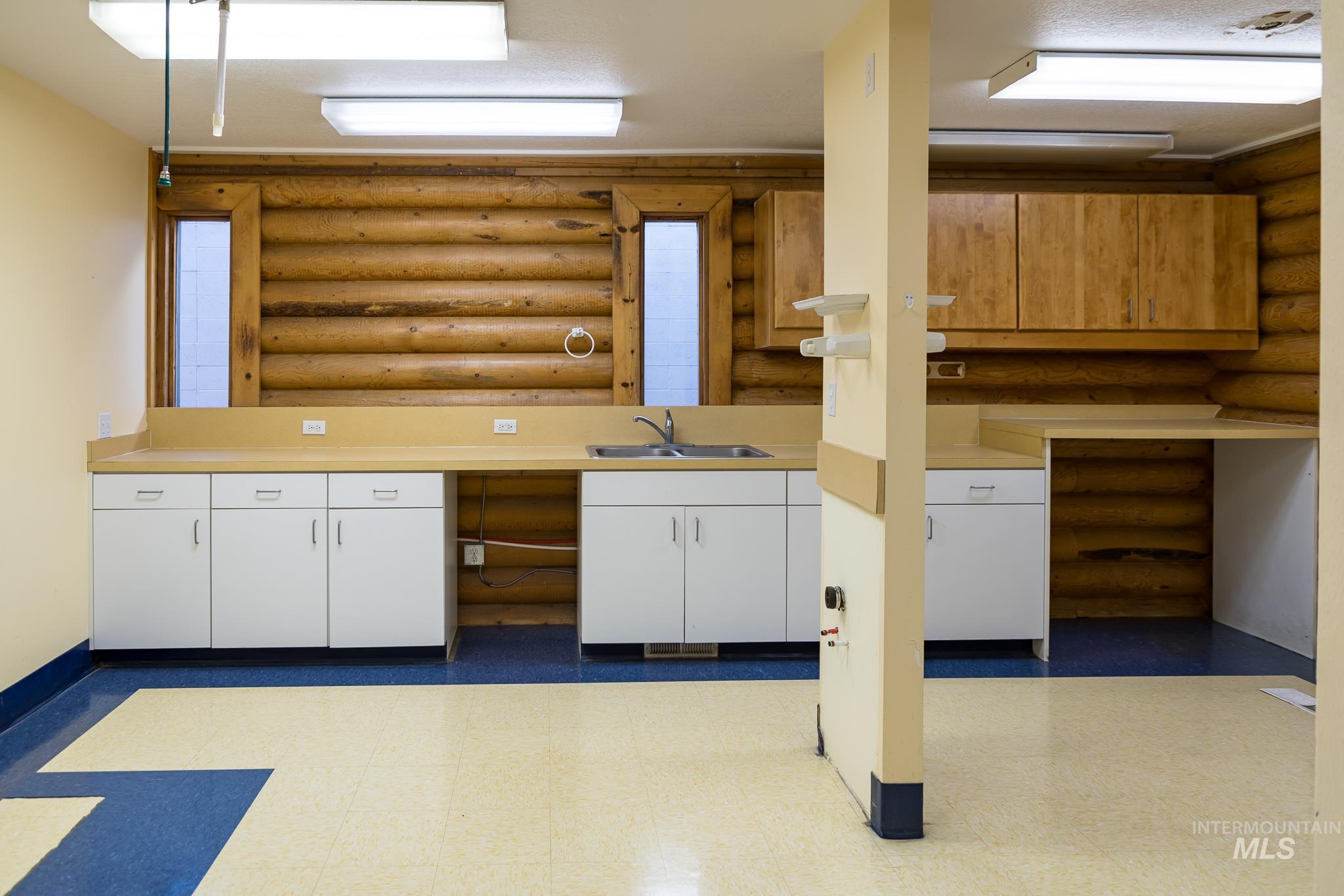 Kitchen featuring white cabinetry, light countertops, light flooring, log walls, and open shelves