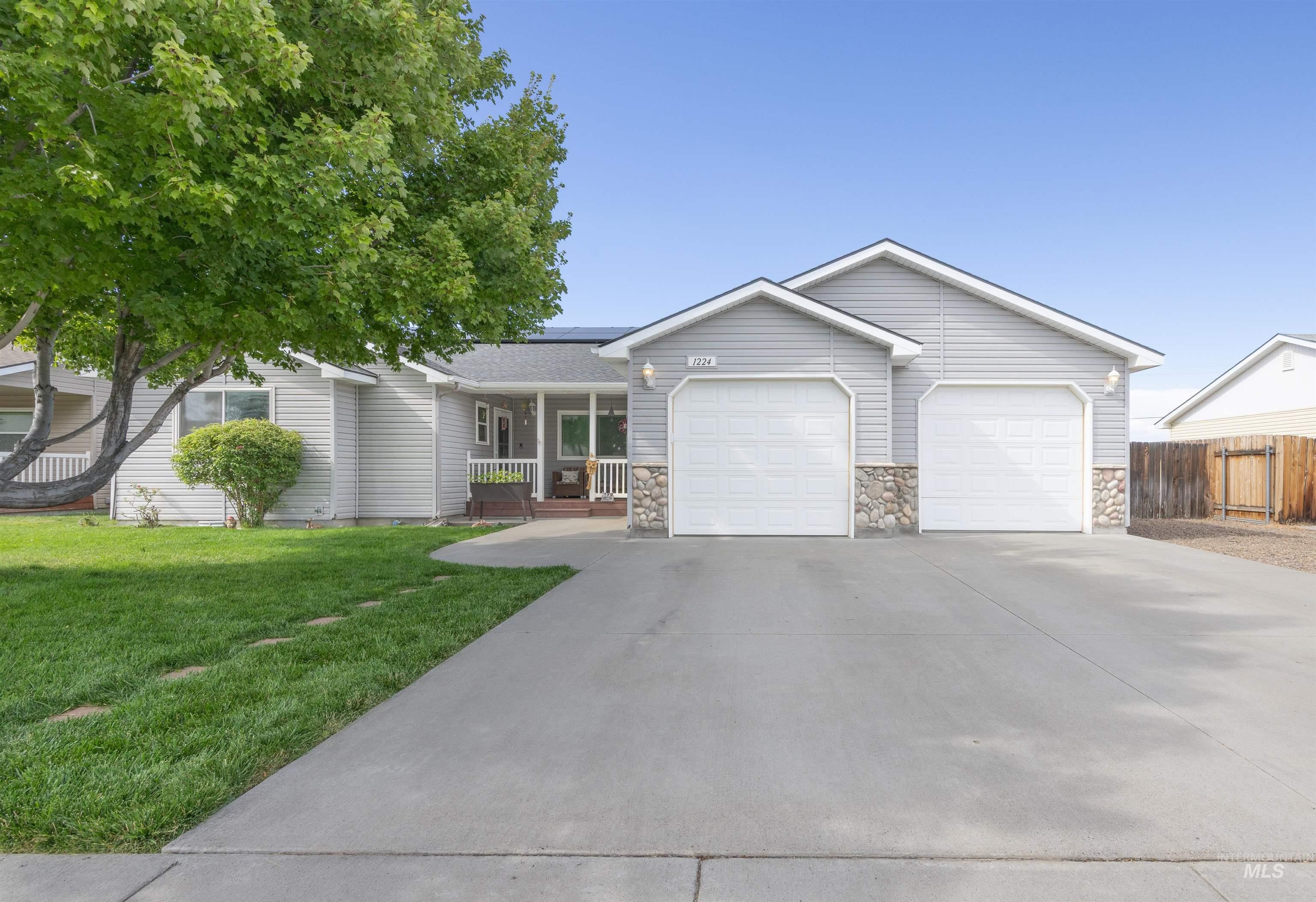 Ranch-style house featuring covered porch, an attached garage, roof mounted solar panels, and concrete driveway