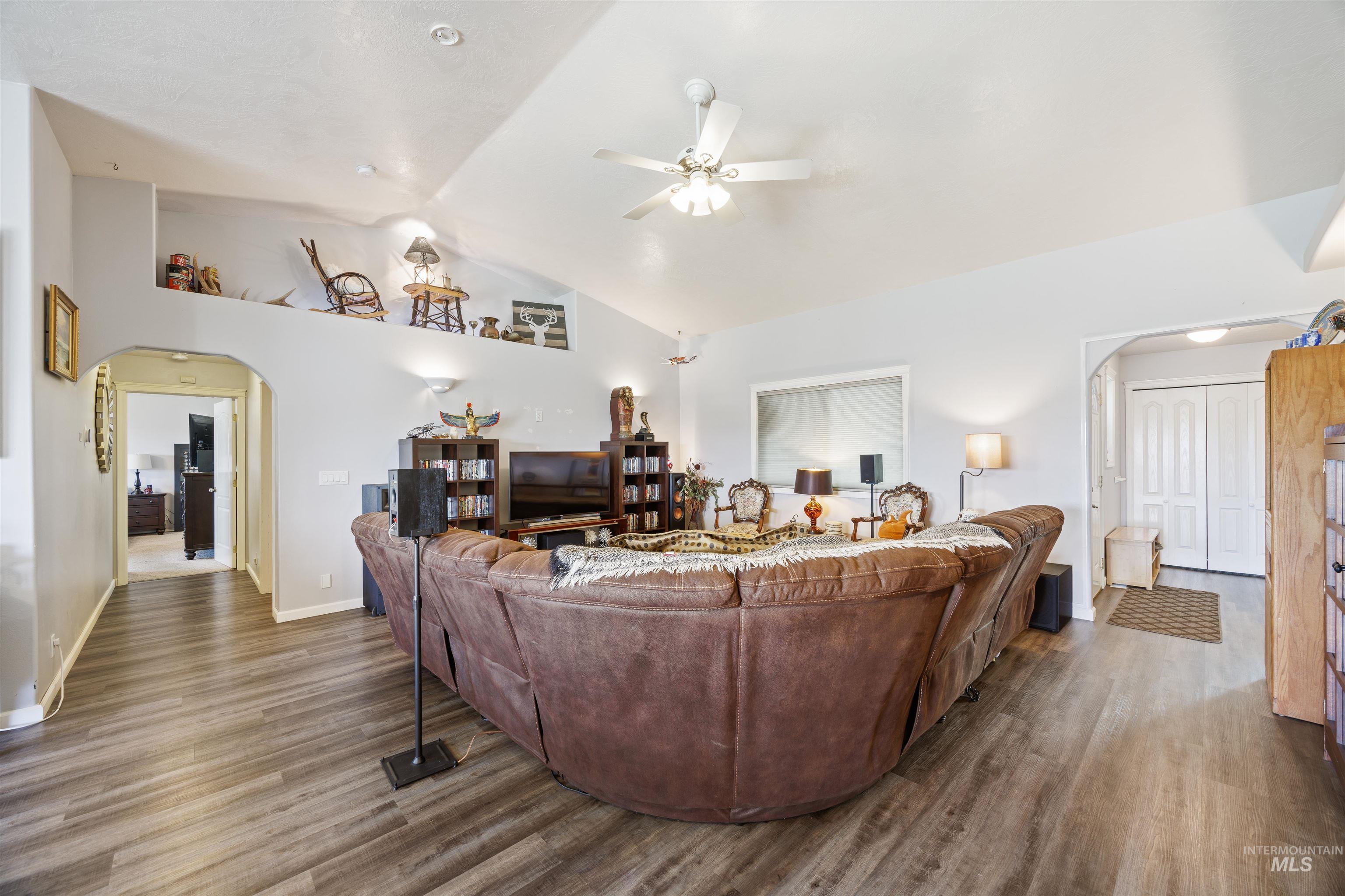 Living room with arched walkways, wood finished floors, a ceiling fan, and high vaulted ceiling