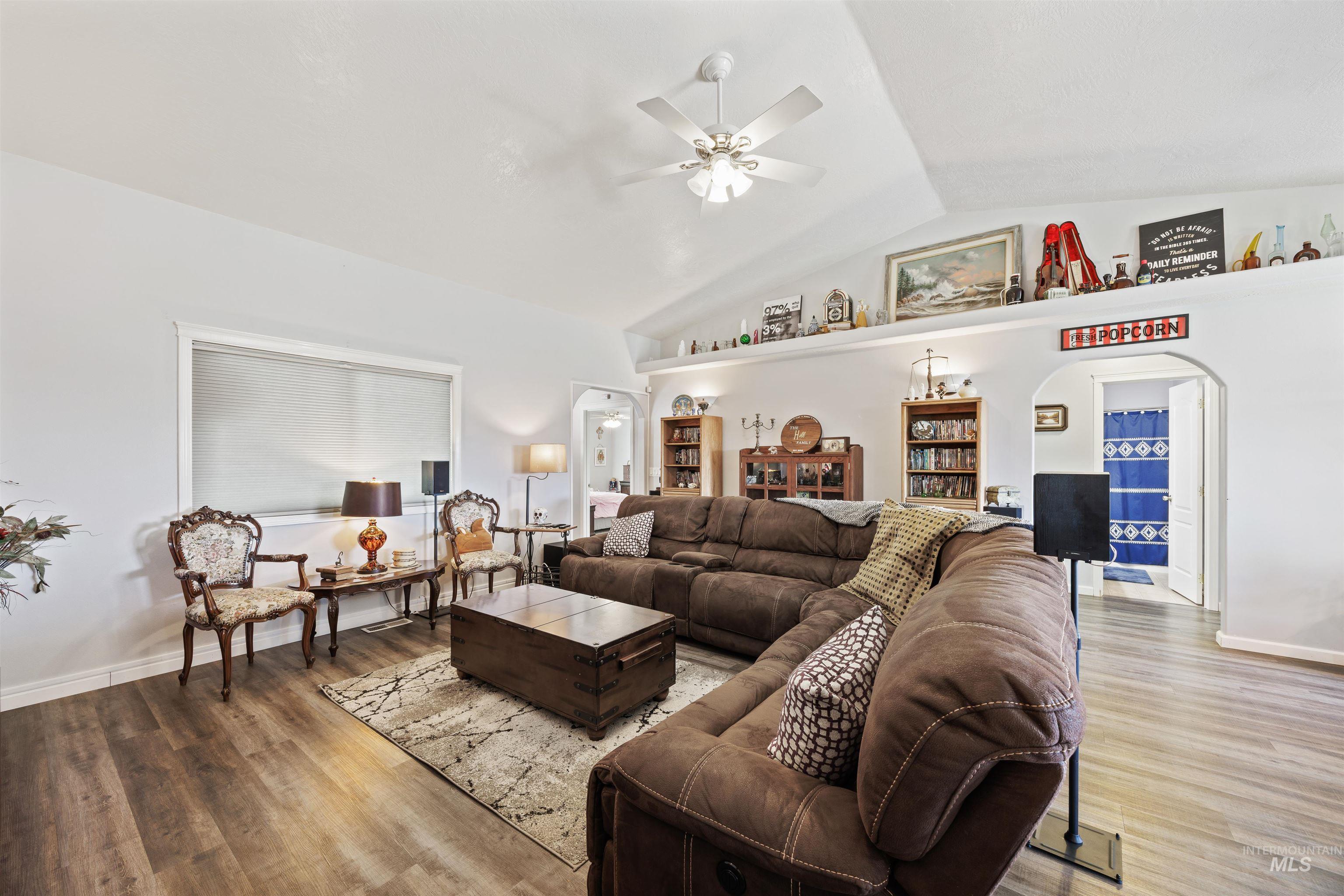 Living room featuring arched walkways, a ceiling fan, vaulted ceiling, and wood finished floors