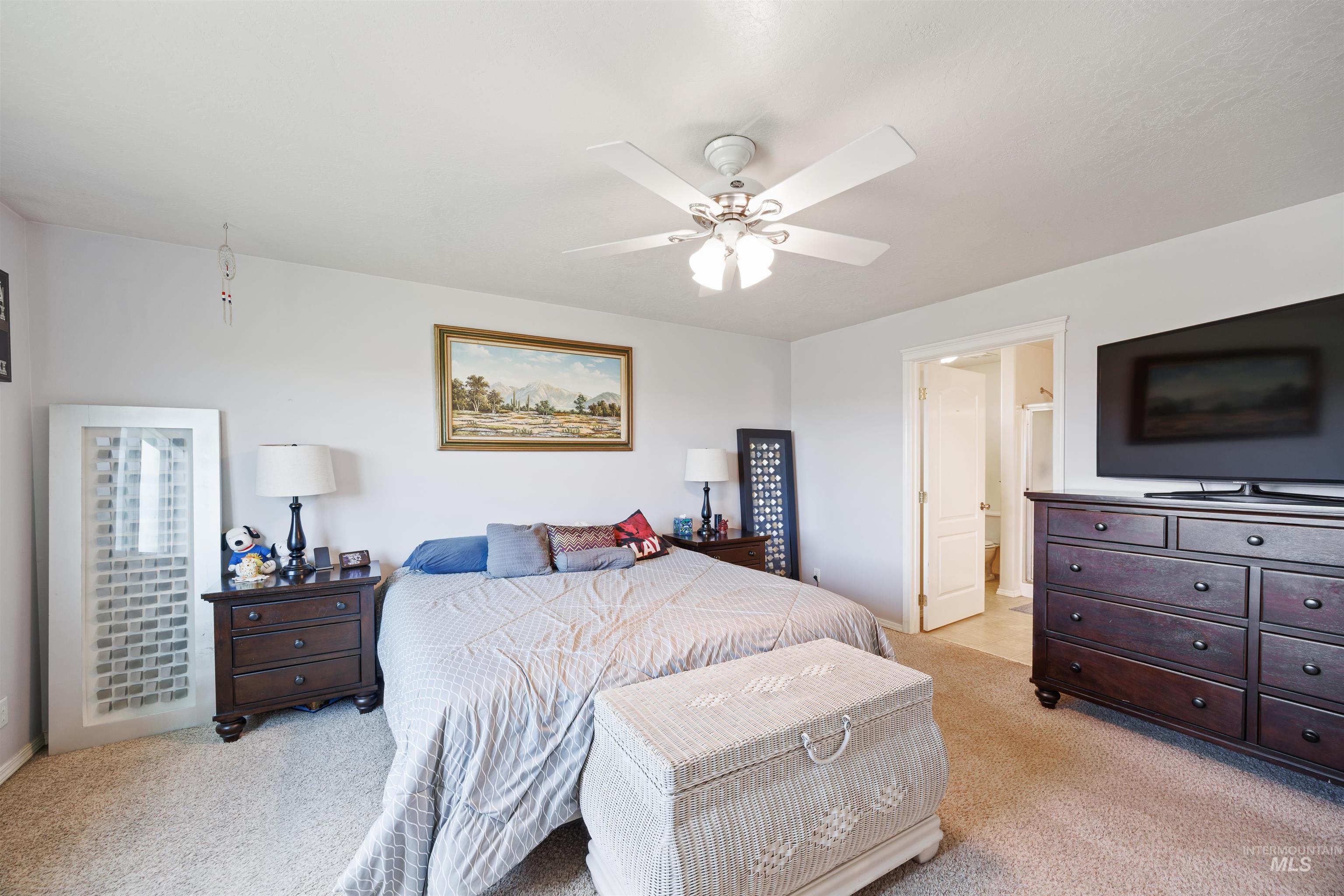 Bedroom with light colored carpet, ceiling fan, and connected bathroom