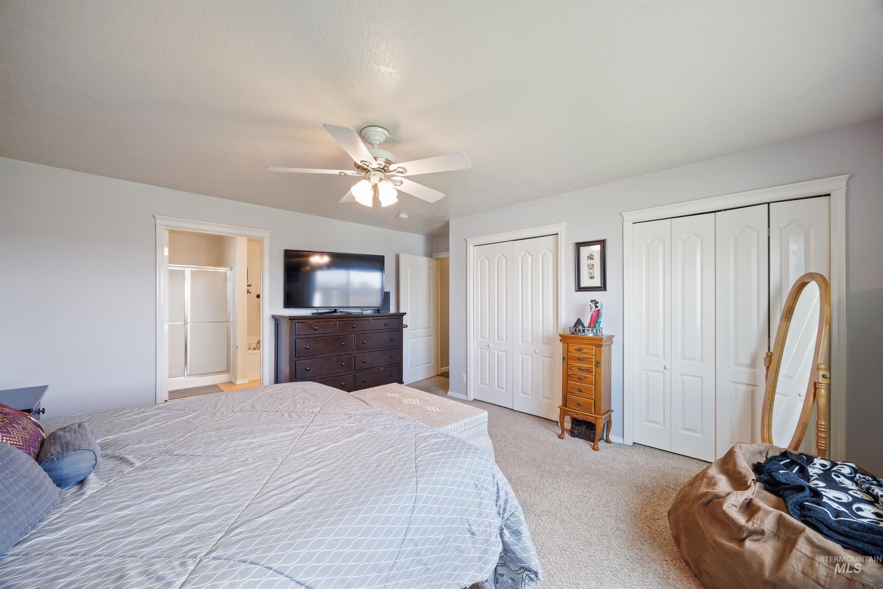 Bedroom with two closets, light colored carpet, and ceiling fan