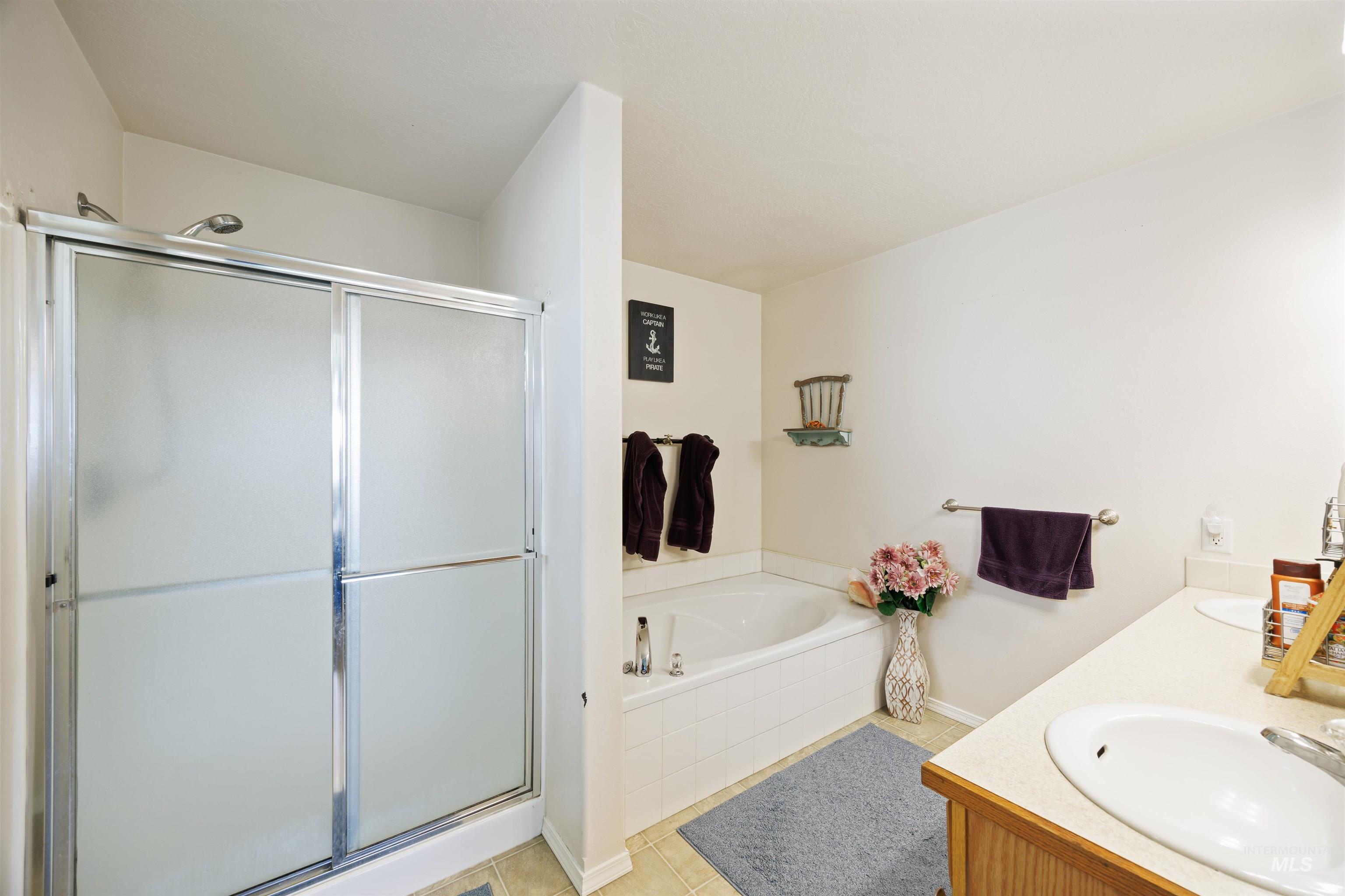 Bathroom featuring a shower stall, a garden tub, tile patterned floors, and double vanity