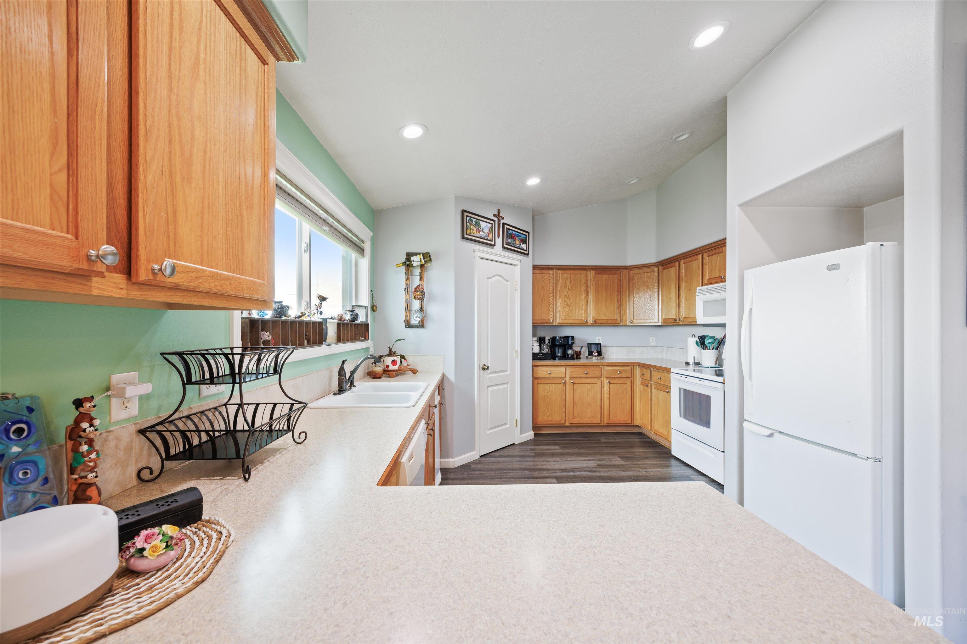 Kitchen featuring white appliances, light countertops, recessed lighting, and dark wood-style floors