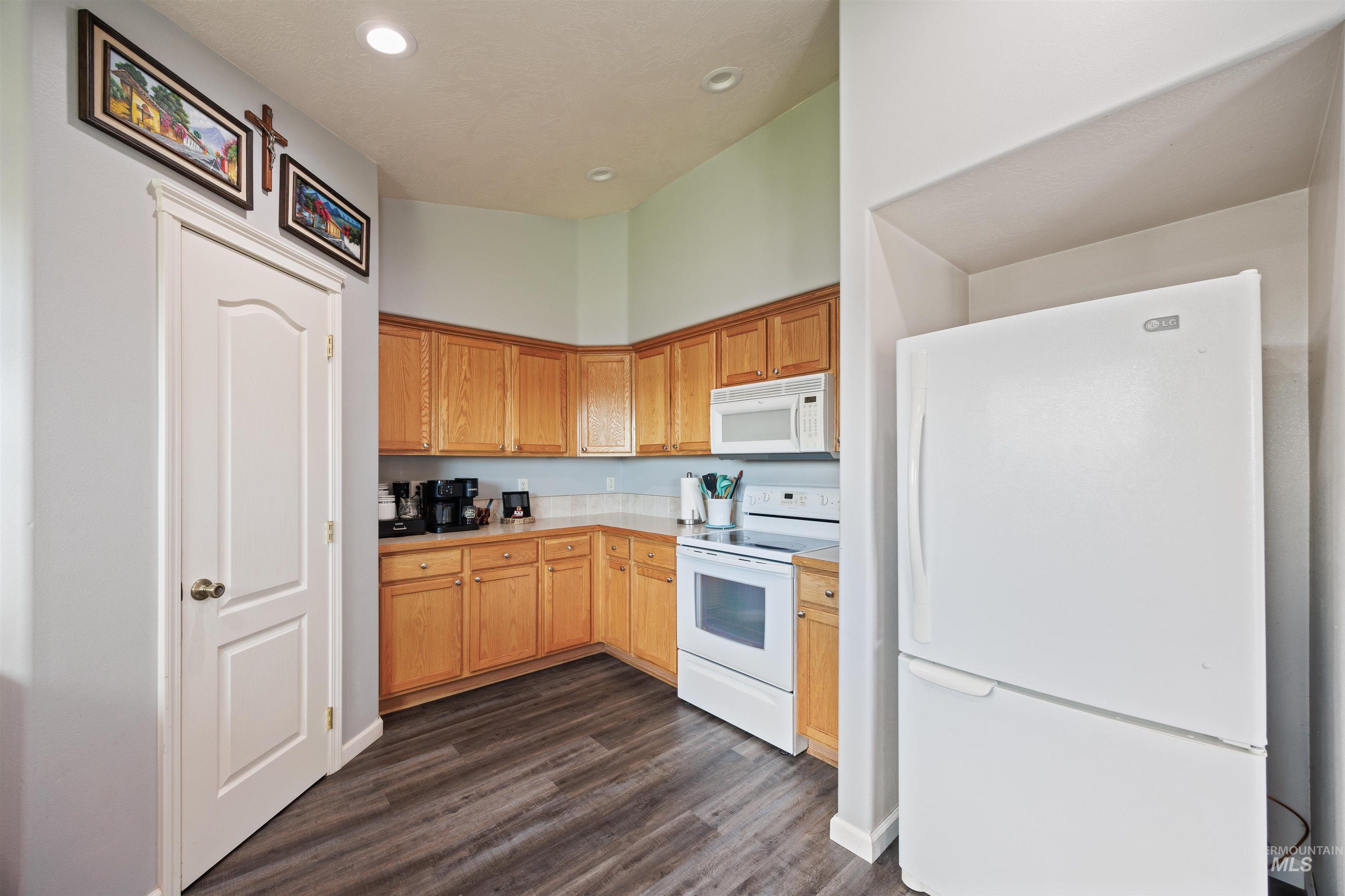 Kitchen with white appliances, dark wood-type flooring, light countertops, and recessed lighting