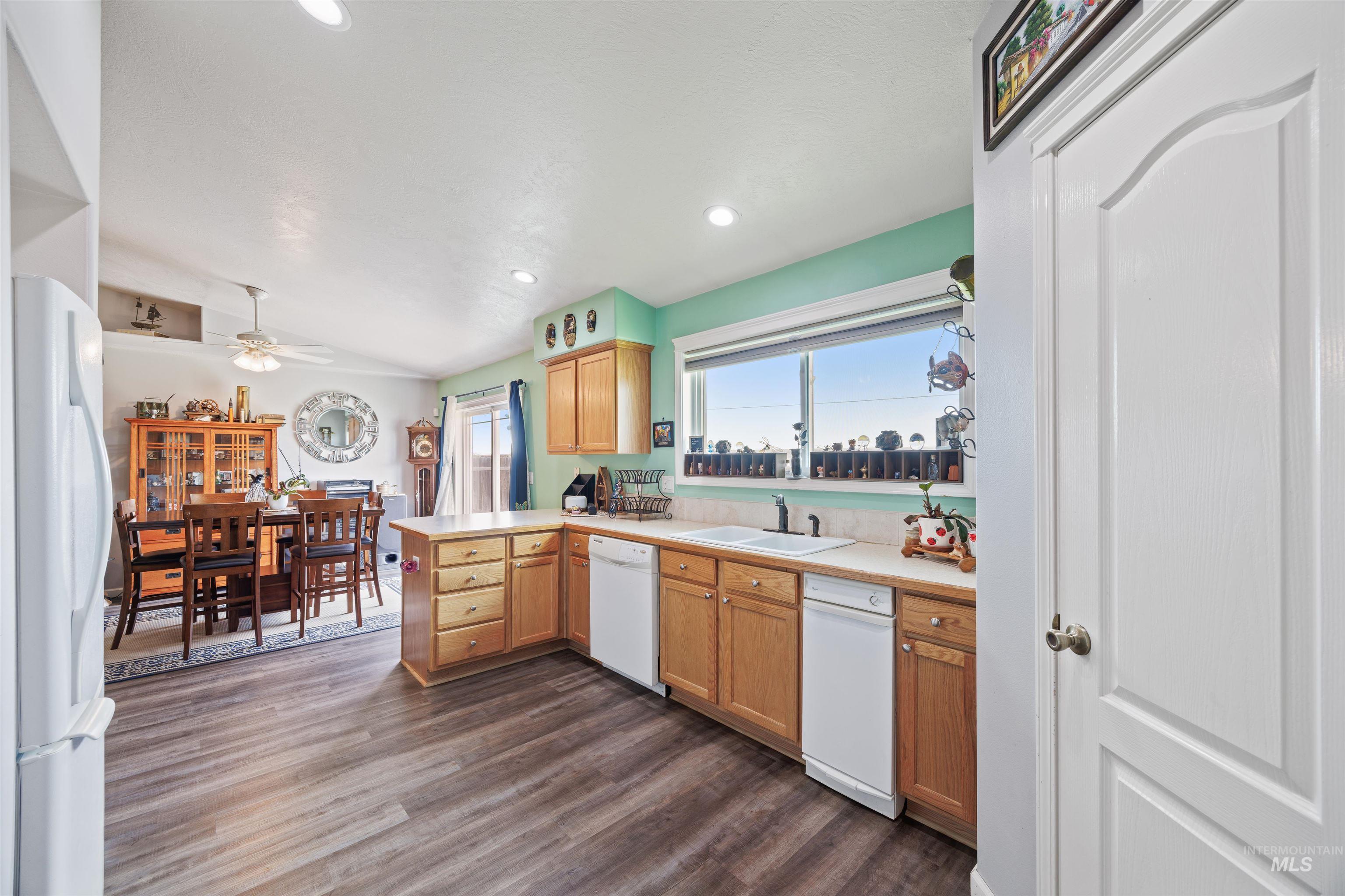 Kitchen with white appliances, dark wood-style flooring, light countertops, lofted ceiling, and a peninsula