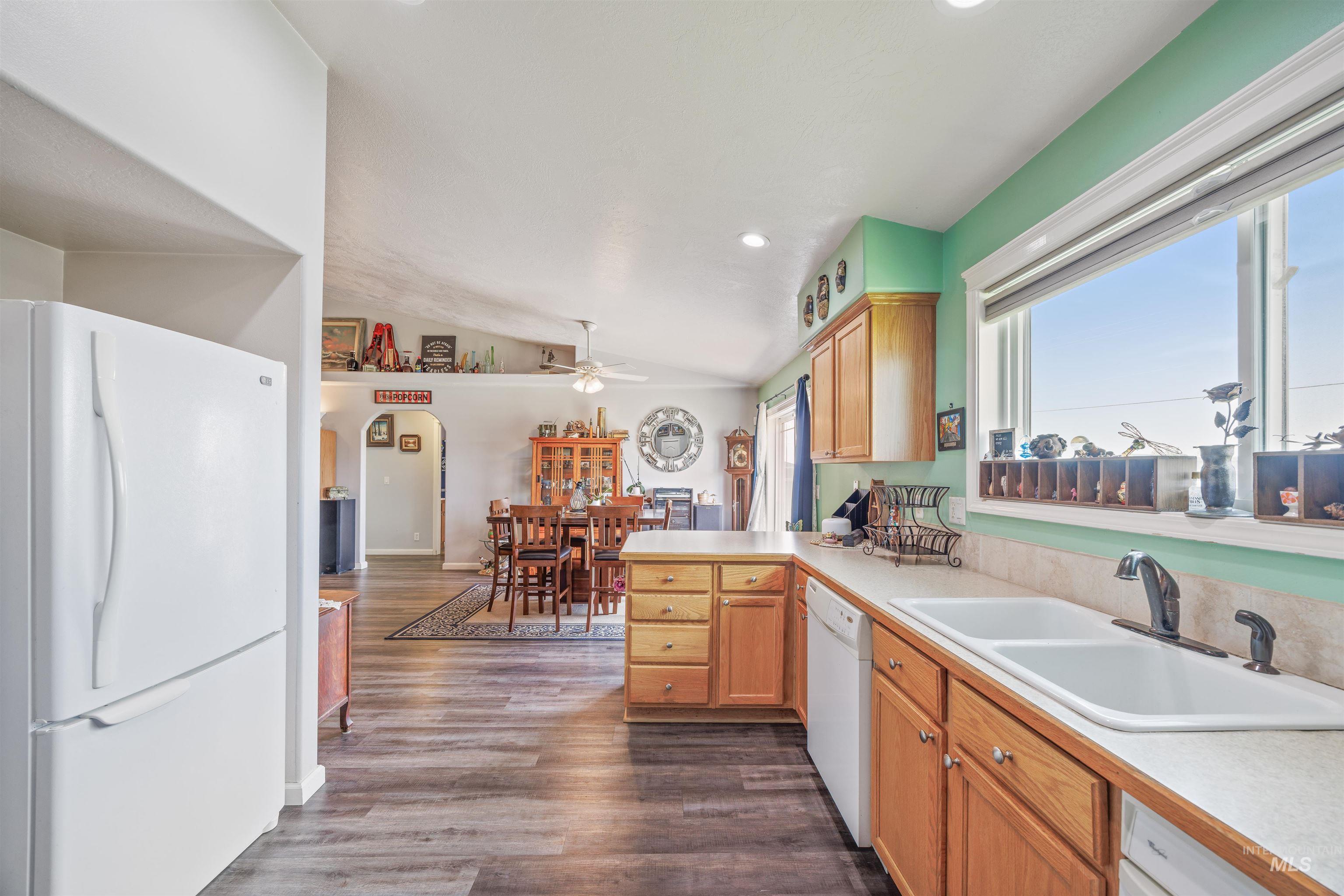 Kitchen with white appliances, arched walkways, vaulted ceiling, dark wood-style floors, and light countertops