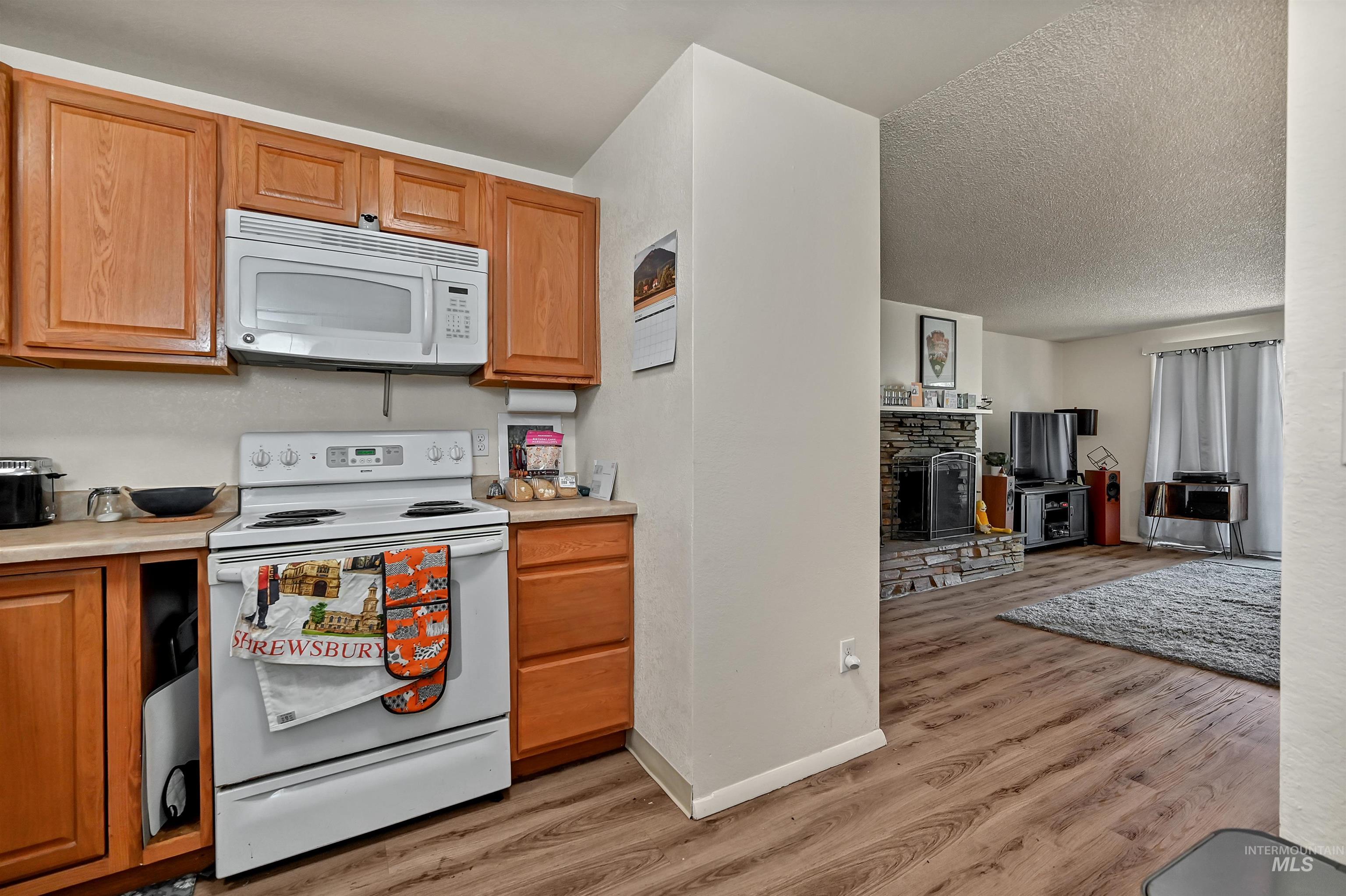 Kitchen with white appliances, light wood finished floors, light countertops, open floor plan, and a textured ceiling