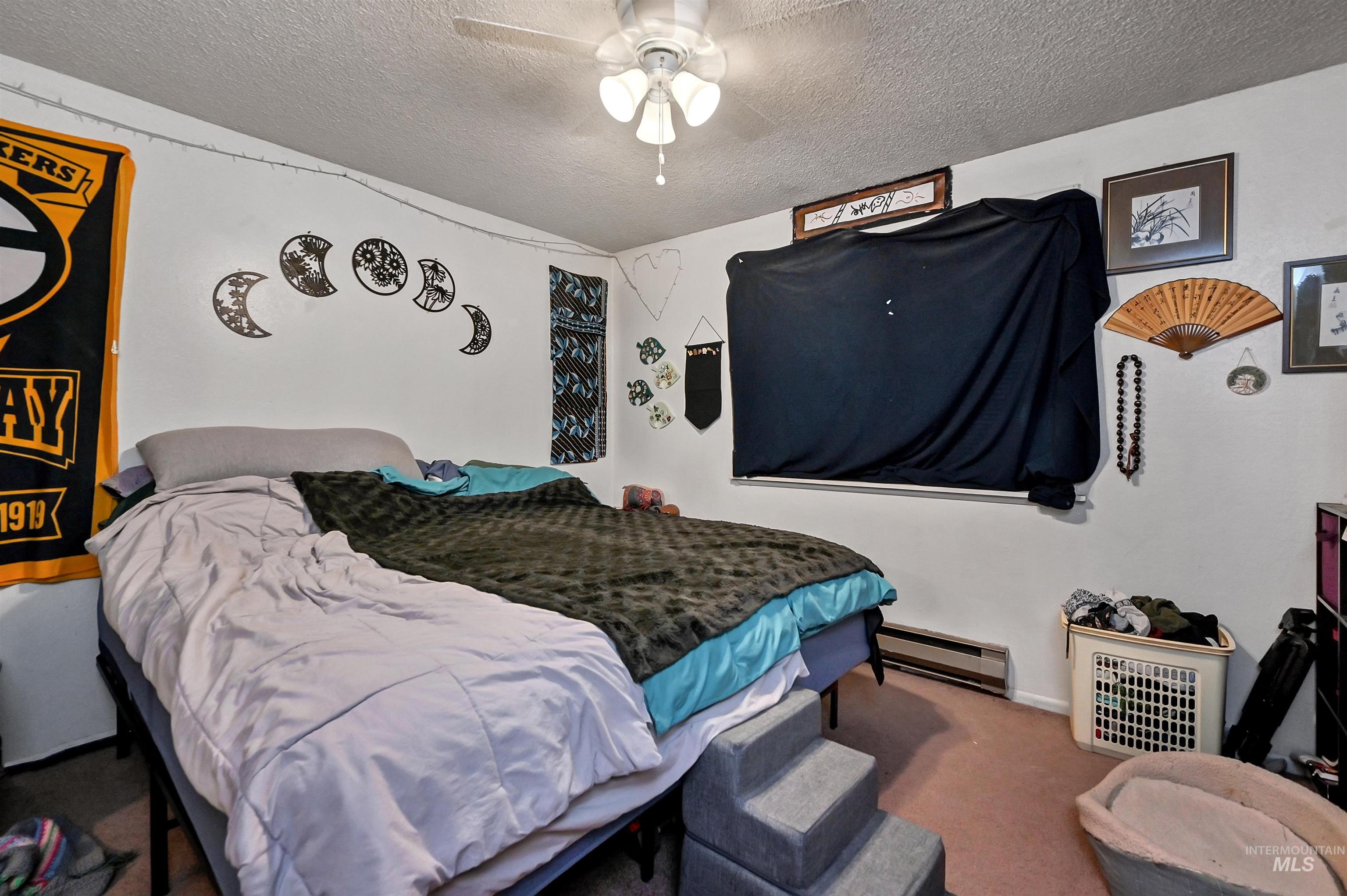 Carpeted bedroom with a textured ceiling, a baseboard radiator, and ceiling fan