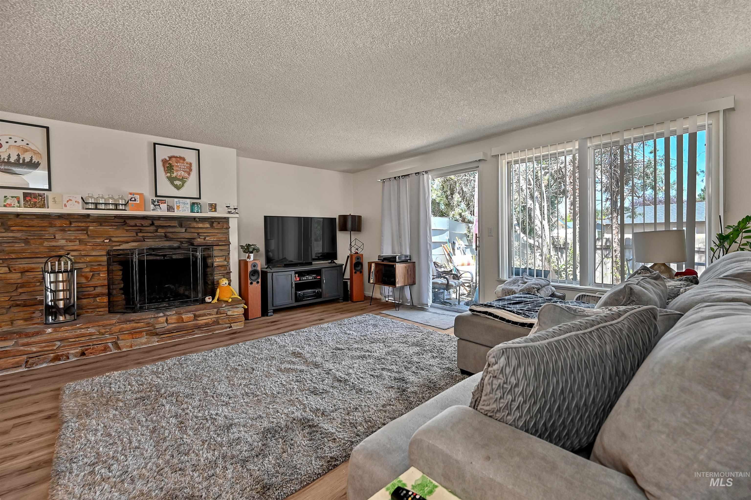 Living area with a stone fireplace, wood finished floors, and a textured ceiling