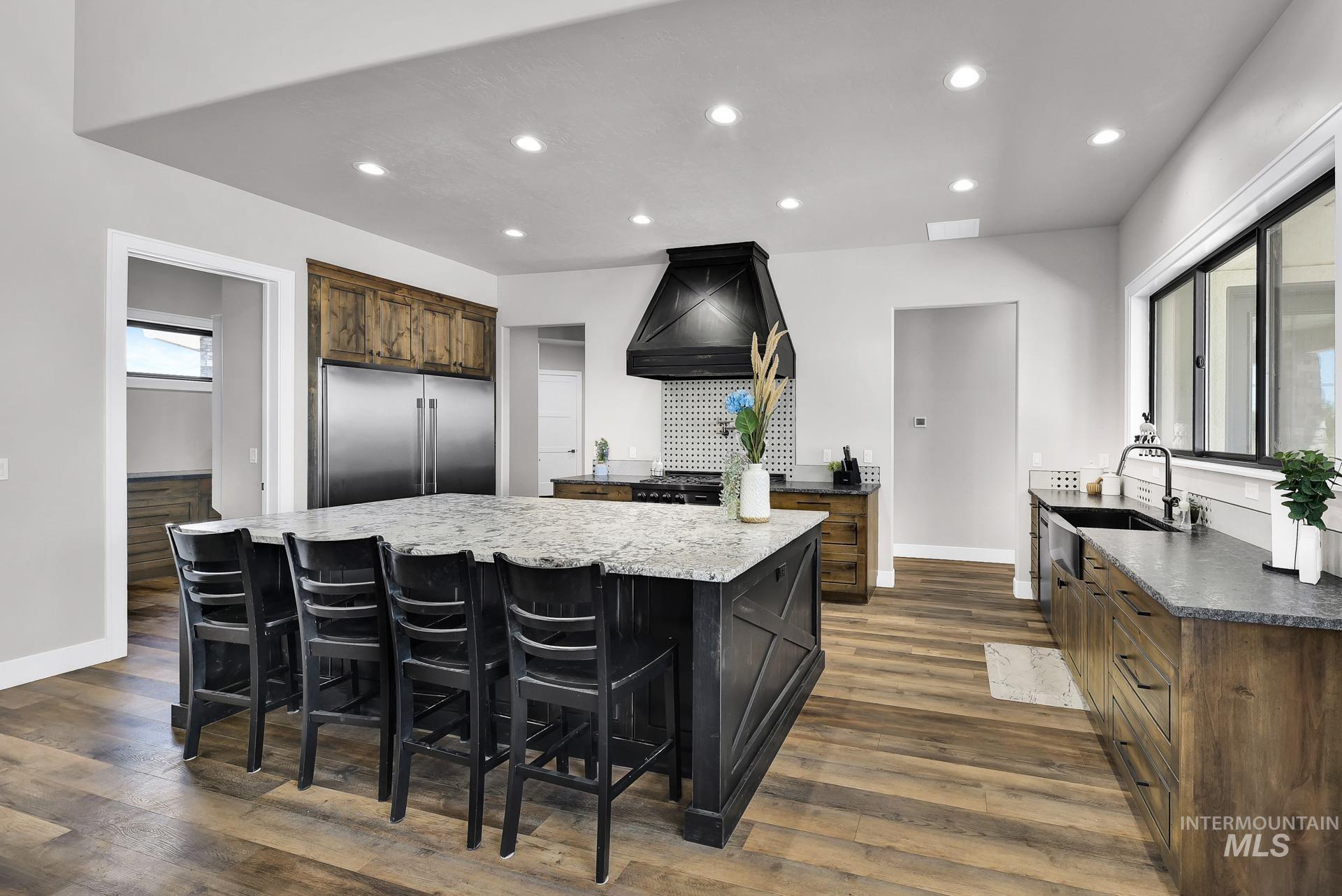 Kitchen featuring recessed lighting, a large island, built in refrigerator, premium range hood, and dark stone counters