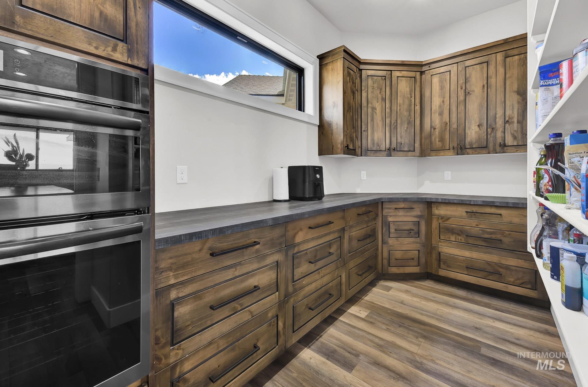 Kitchen with double oven, dark countertops, dark wood-type flooring, and dark brown cabinetry