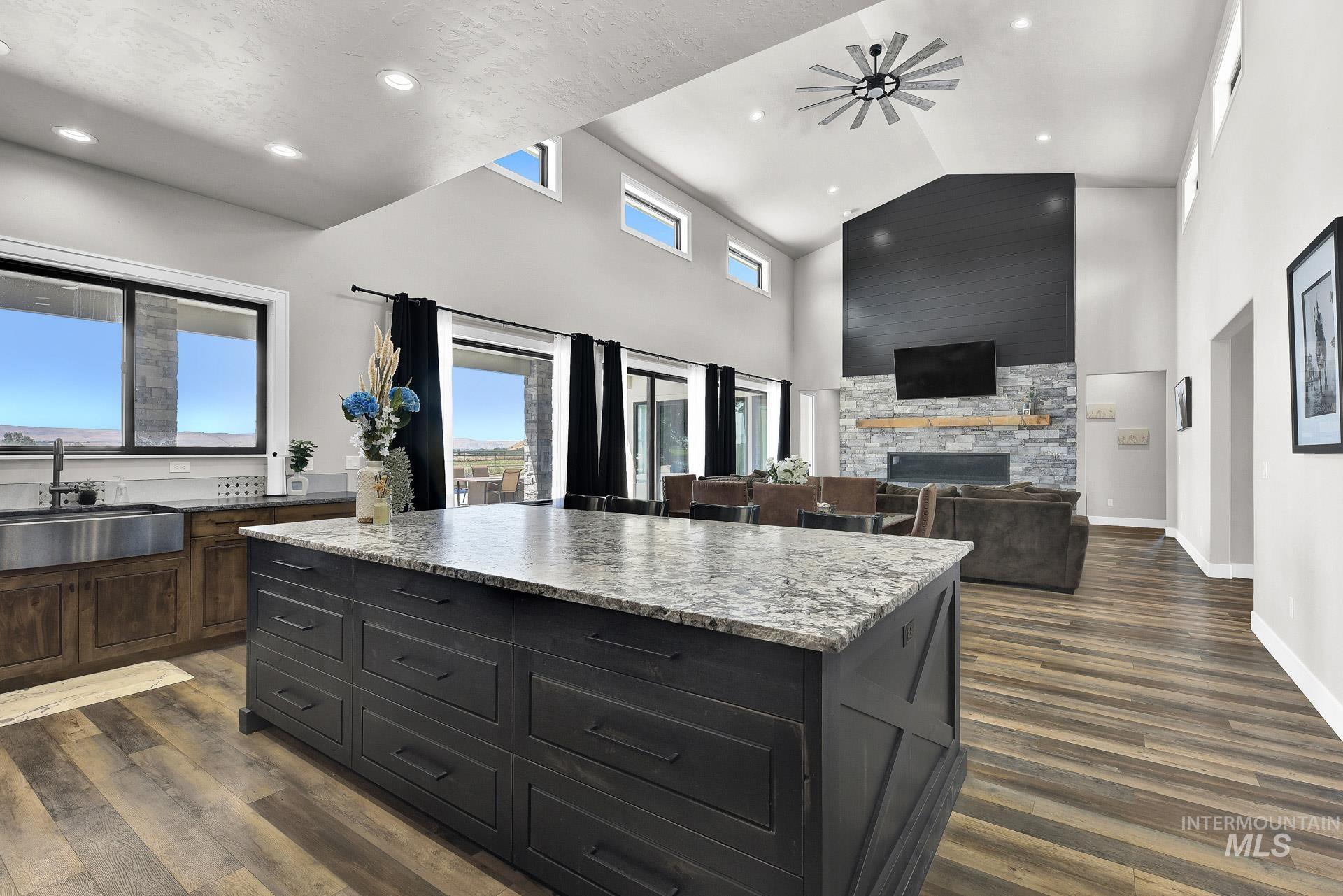 Kitchen with dark wood-type flooring, a stone fireplace, recessed lighting, a center island, and high vaulted ceiling