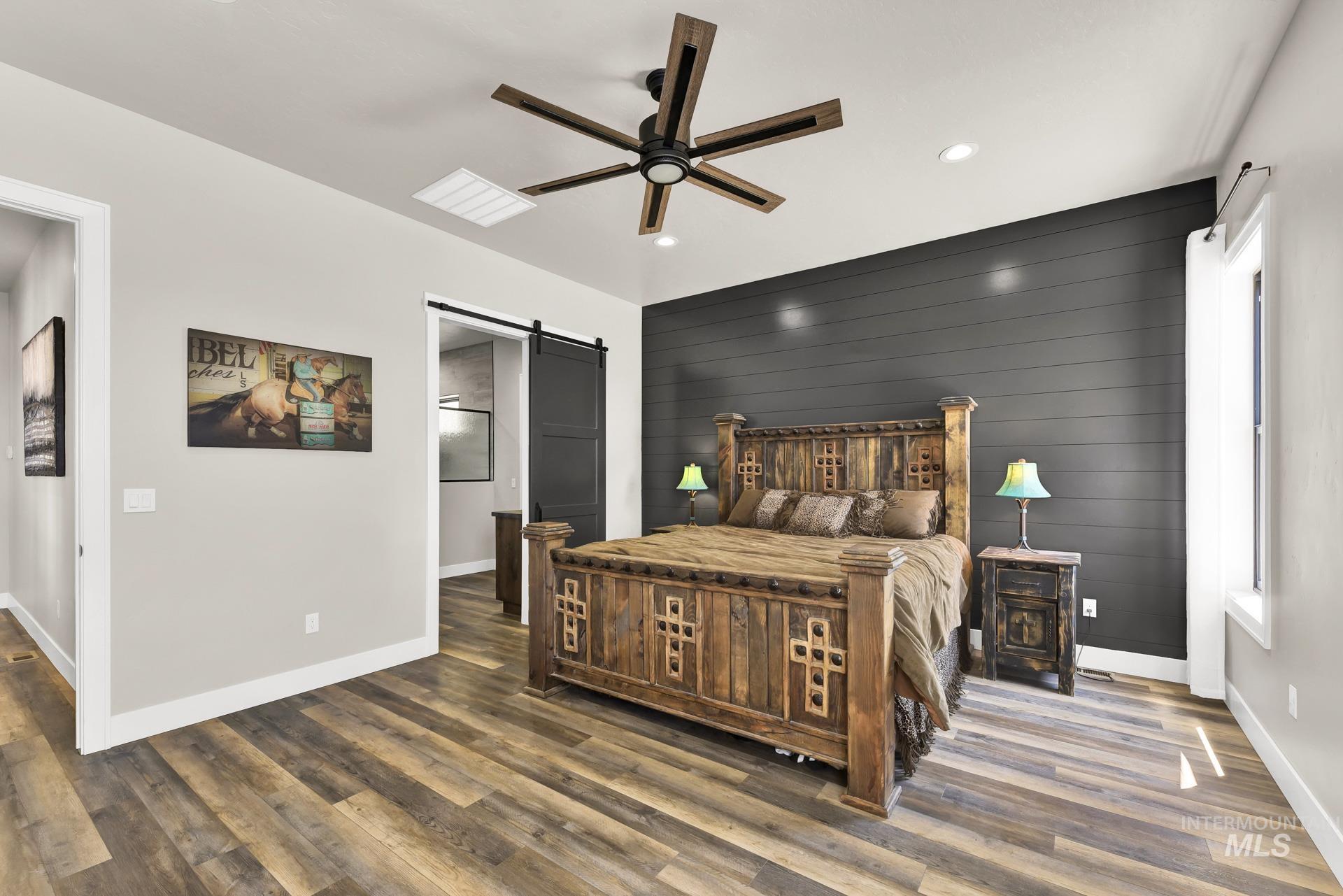 Bedroom featuring a barn door, wooden walls, wood finished floors, ceiling fan, and recessed lighting