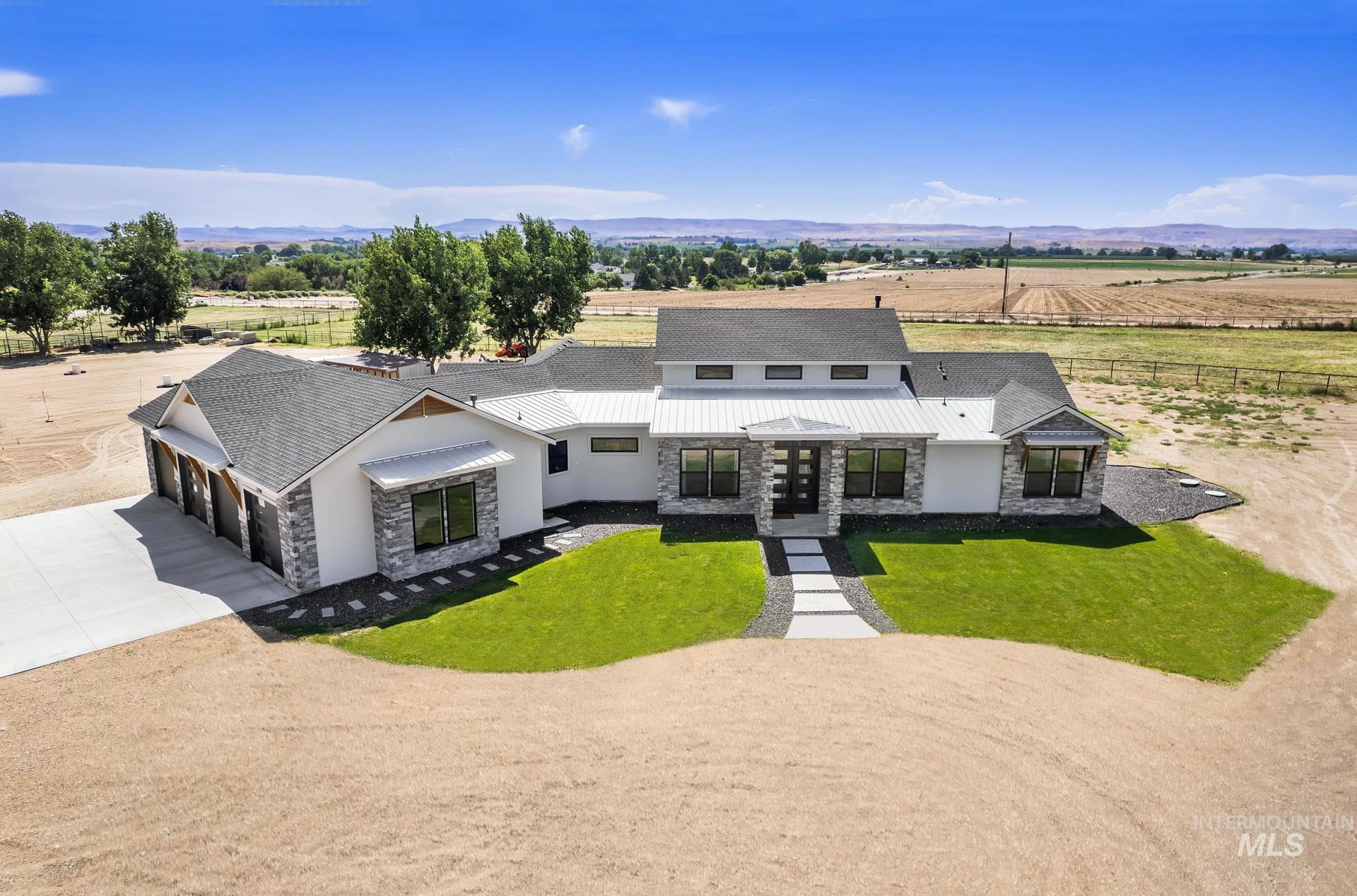 Modern farmhouse with stone siding, concrete driveway, a rural view, and an attached garage