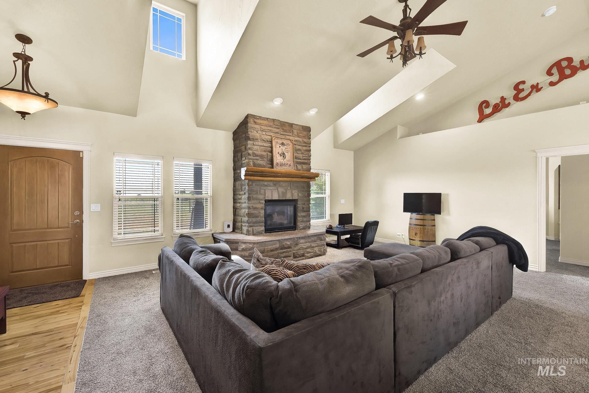 Living room featuring a stone fireplace, high vaulted ceiling, a ceiling fan, recessed lighting, and light colored carpet