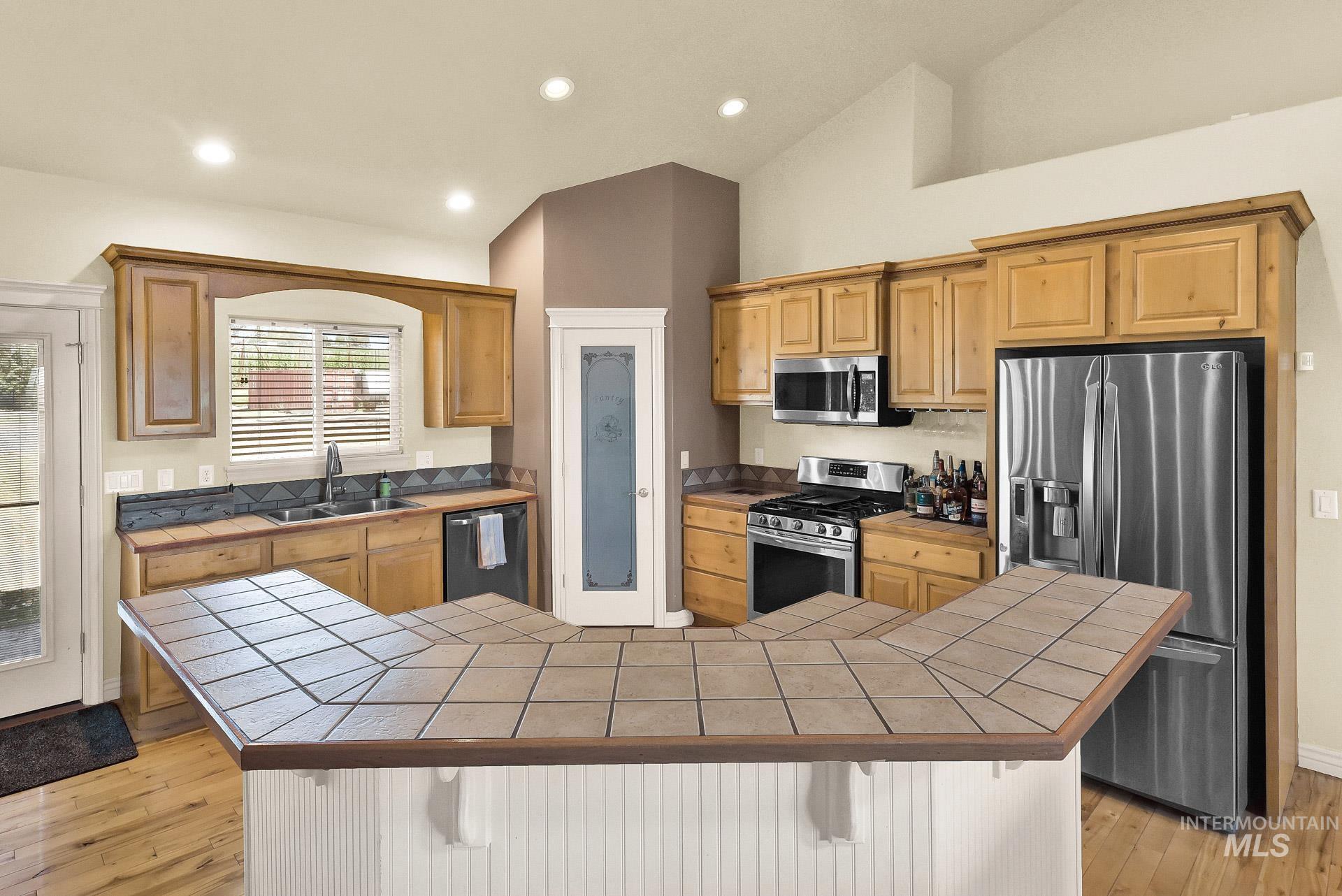 Kitchen featuring tile countertops, a kitchen bar, vaulted ceiling, stainless steel appliances, and light wood-style flooring