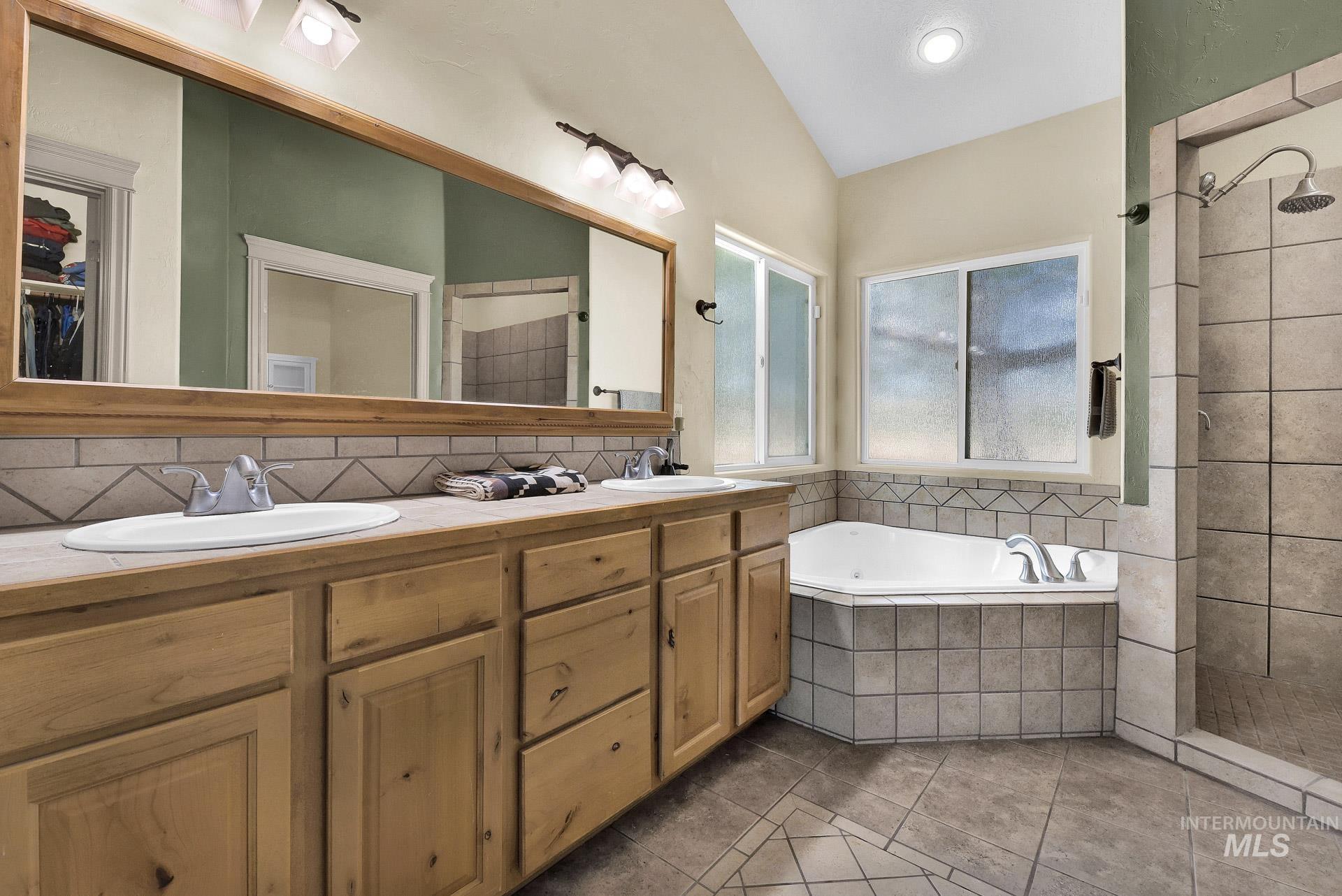 Full bath featuring tile patterned flooring, a garden tub, double vanity, tiled shower, and lofted ceiling