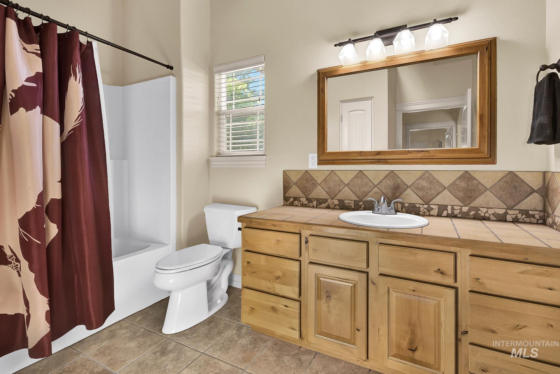 Full bath featuring vanity, tasteful backsplash, tile patterned flooring, and shower / tub combo with curtain
