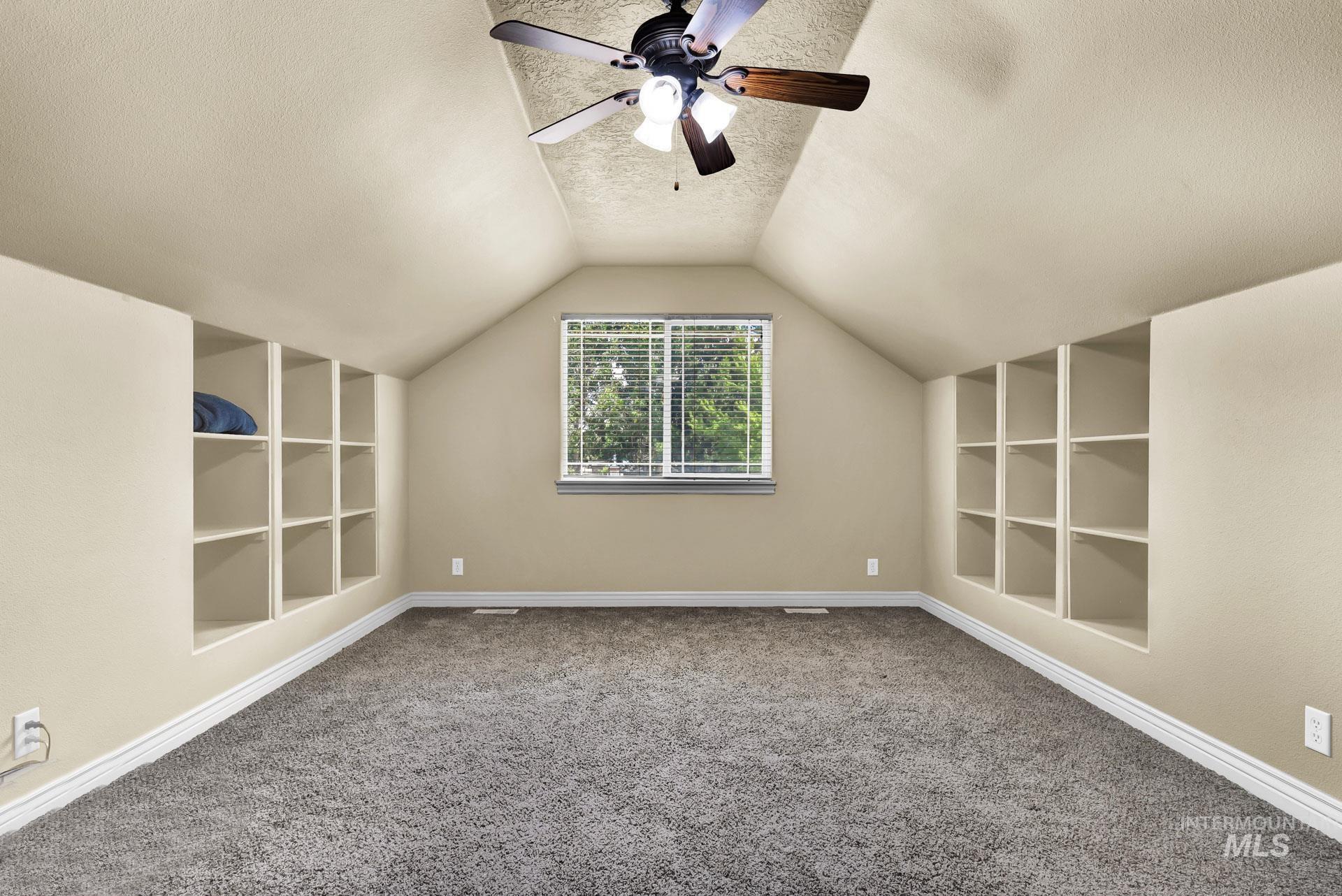 Bonus room featuring built in features, a textured ceiling, lofted ceiling, carpet, and a ceiling fan