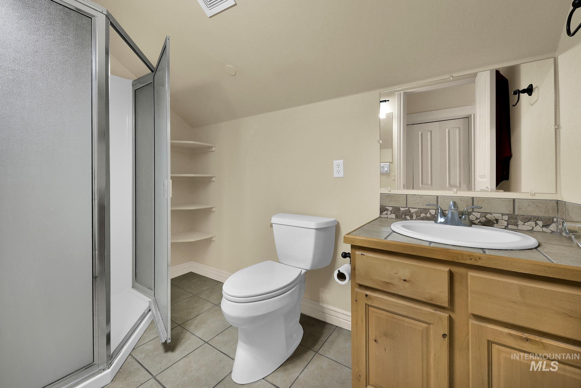 Full bath with tile patterned flooring, a stall shower, vanity, and lofted ceiling