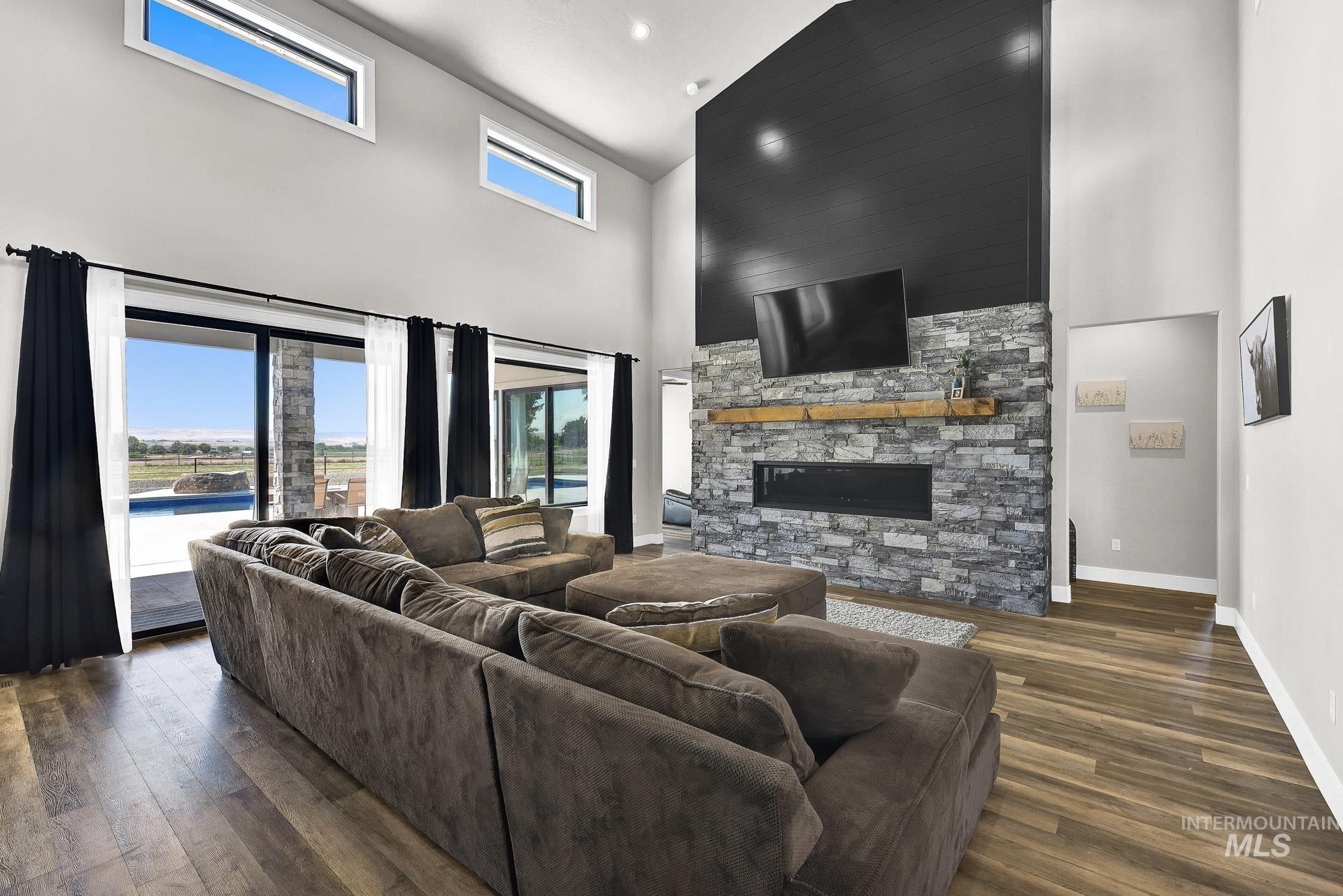 Living area with wood finished floors, a towering ceiling, a stone fireplace, and recessed lighting