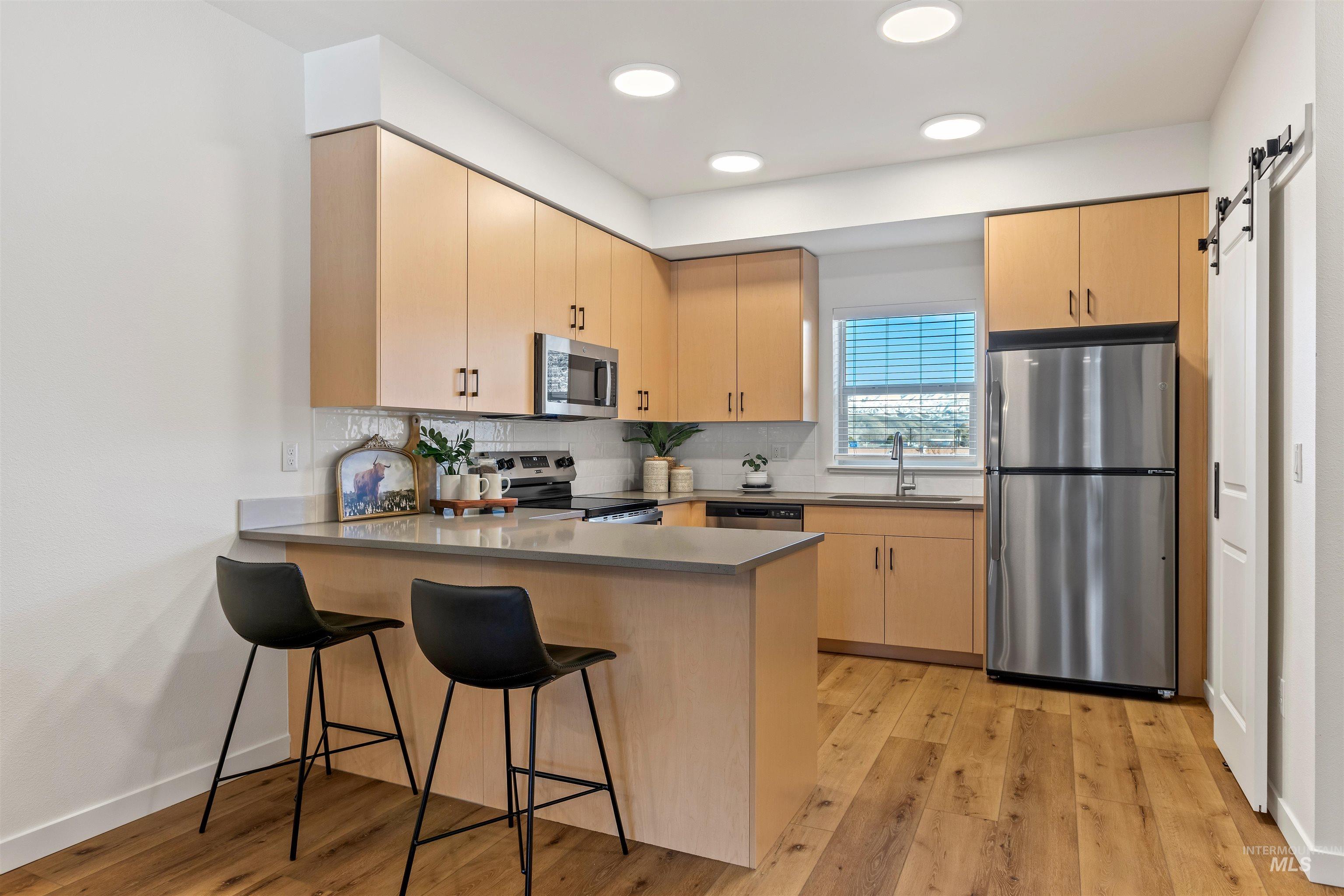 Kitchen featuring a barn door, appliances with stainless steel finishes, a peninsula, backsplash, and light wood-type flooring