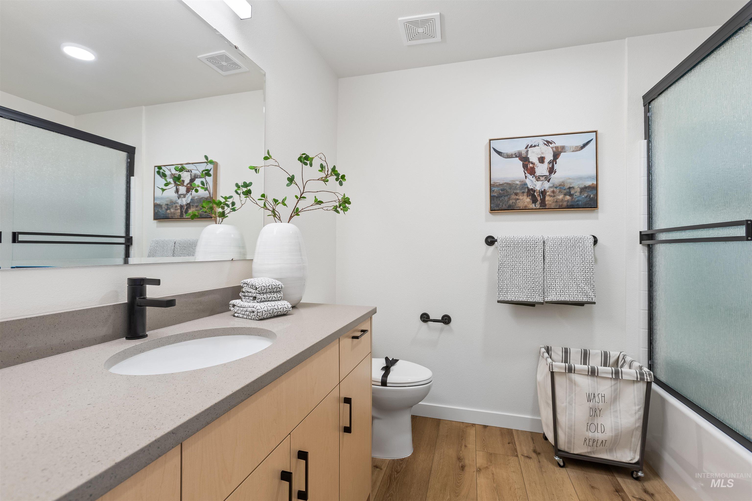 Full bathroom featuring wood finished floors, vanity, and combined bath / shower with glass door