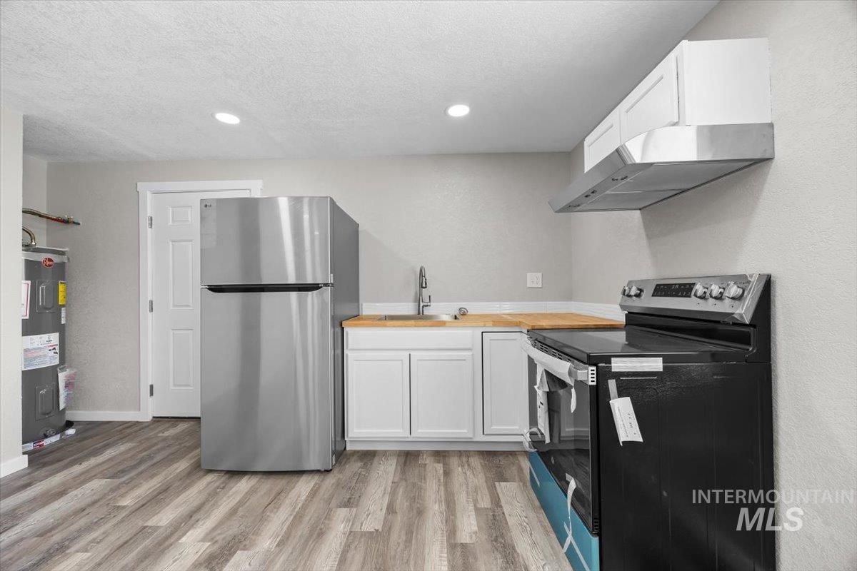 Kitchen featuring range with electric stovetop, freestanding refrigerator, range hood, butcher block counters, and light wood-type flooring