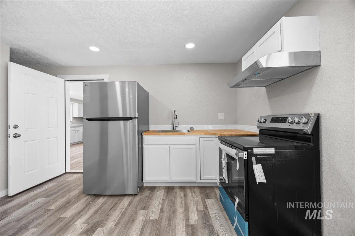 Kitchen featuring range with electric cooktop, freestanding refrigerator, butcher block countertops, ventilation hood, and light wood finished floors