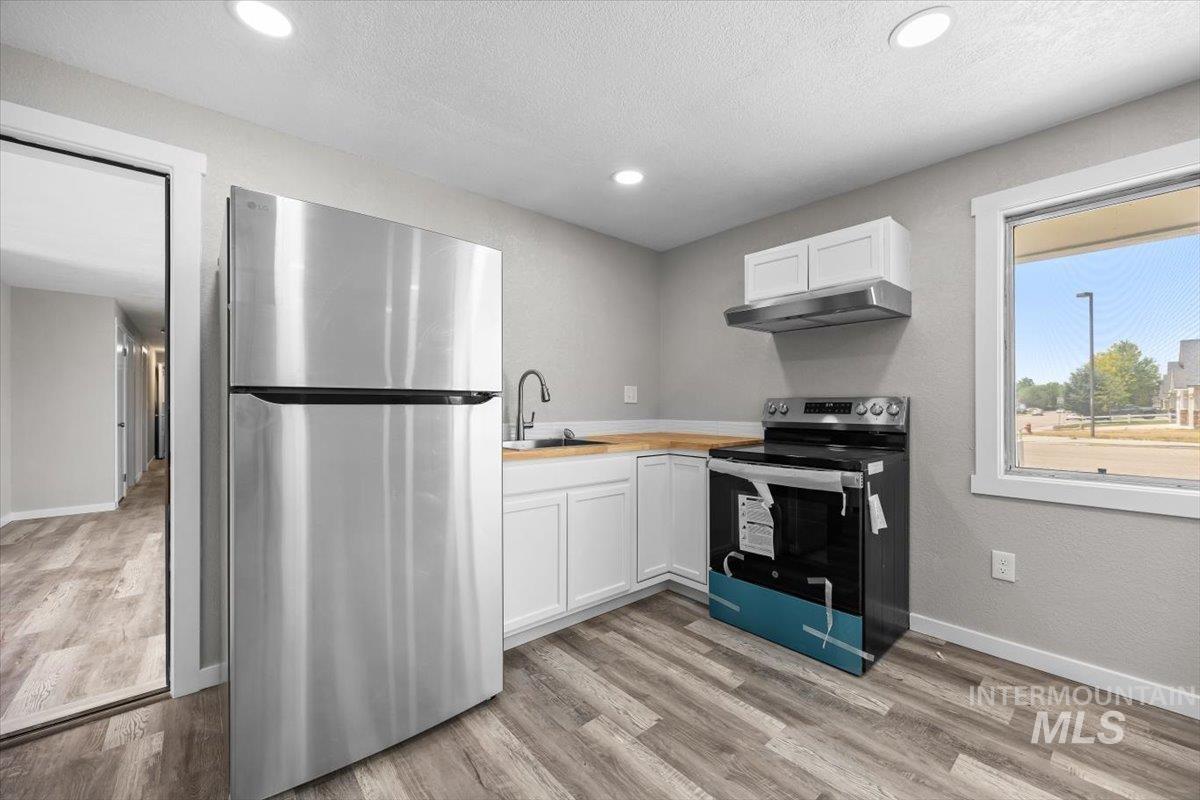 Kitchen featuring stainless steel appliances, under cabinet range hood, light wood-type flooring, white cabinets, and light countertops