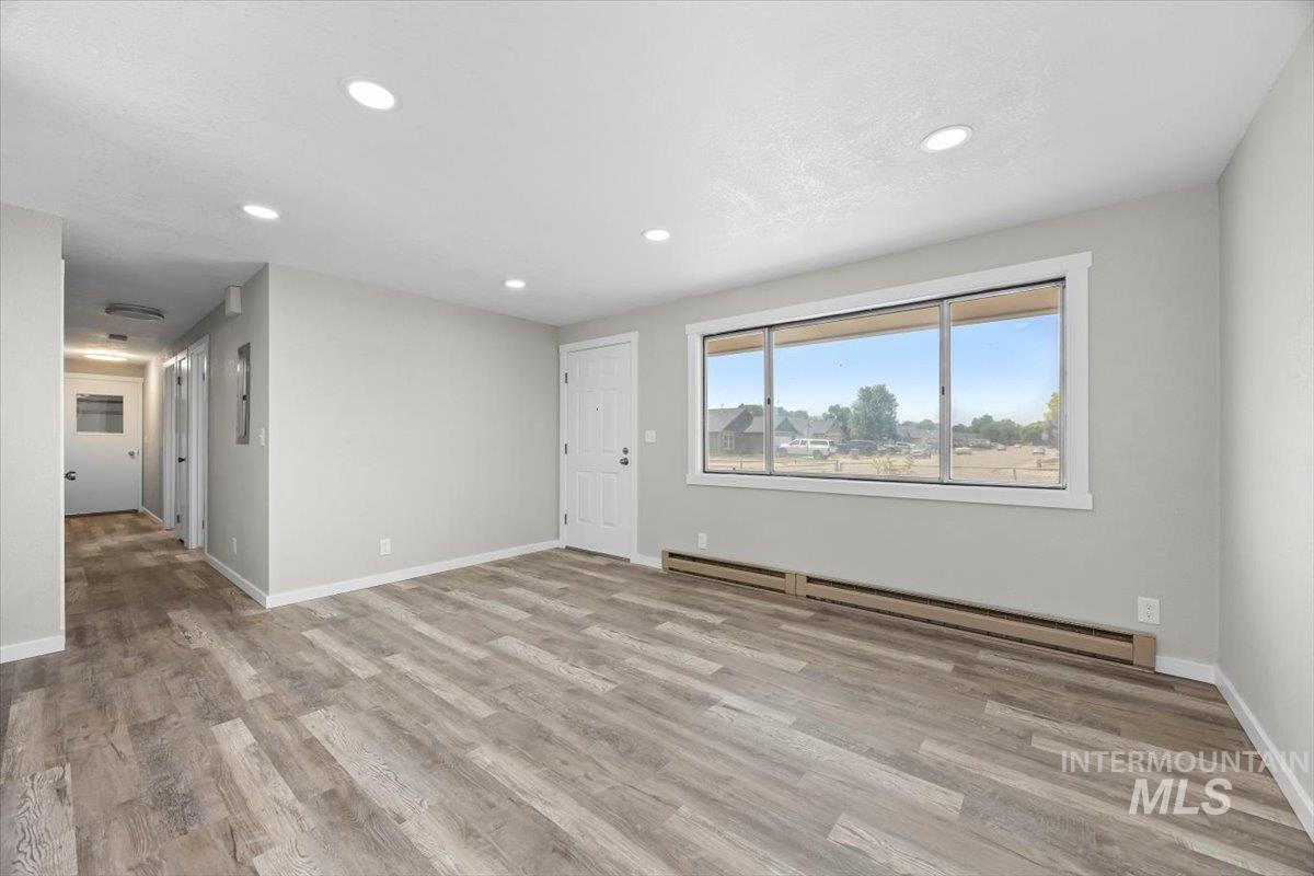 Unfurnished living room featuring a baseboard radiator, recessed lighting, and wood finished floors