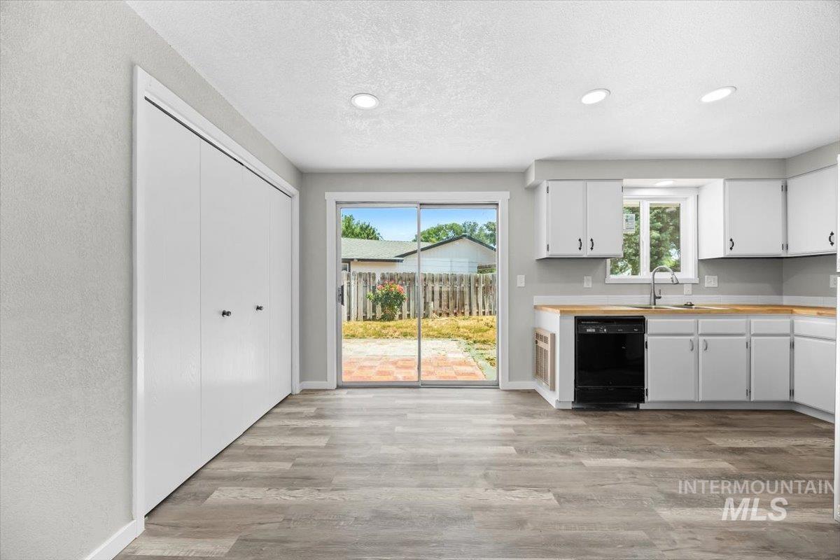 Kitchen with black dishwasher, light wood-style flooring, a textured ceiling, white cabinets, and recessed lighting
