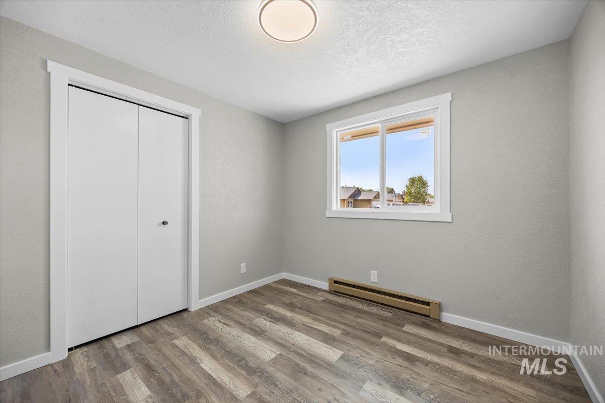 Unfurnished bedroom with a baseboard heating unit, wood finished floors, a textured ceiling, a closet, and a textured wall
