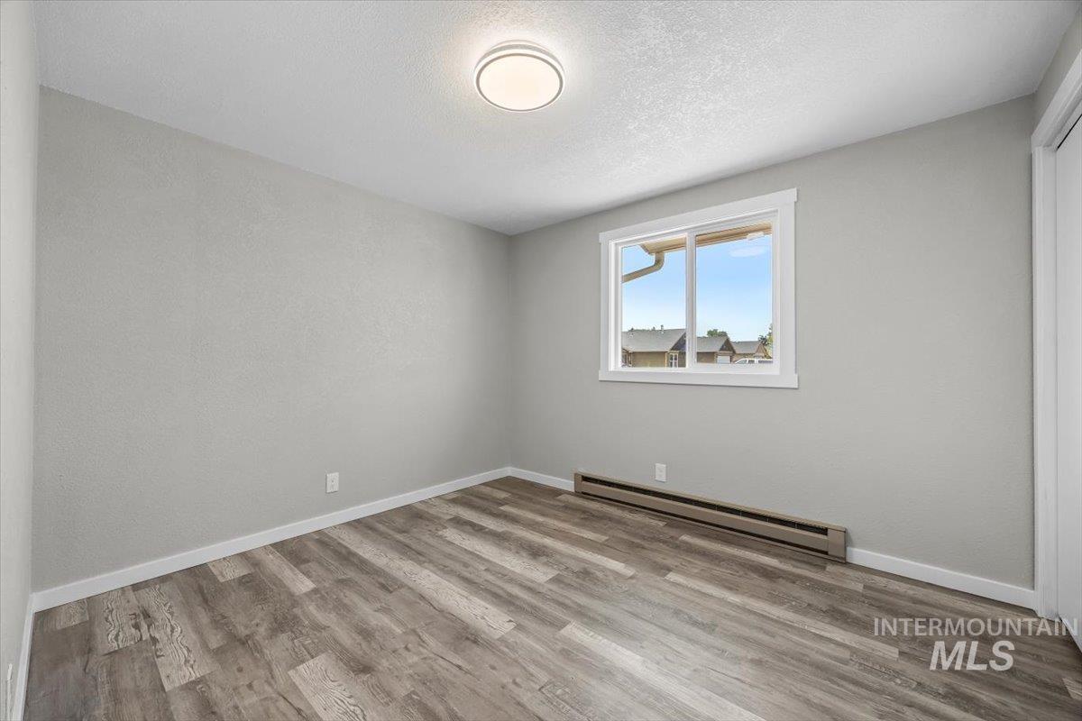 Unfurnished bedroom featuring a baseboard heating unit, wood finished floors, a textured ceiling, and a closet