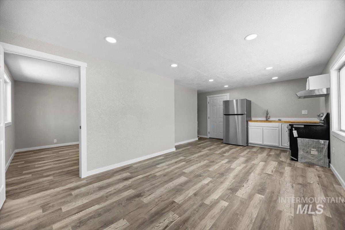Kitchen featuring light wood-type flooring, freestanding refrigerator, stove, a textured ceiling, and recessed lighting