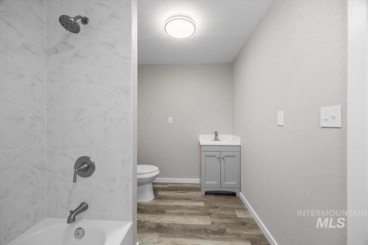 Bathroom featuring a textured ceiling, wood finished floors, vanity, and tub / shower combination