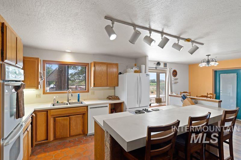 Kitchen with track lighting, a textured ceiling, white appliances, a kitchen breakfast bar, and light countertops