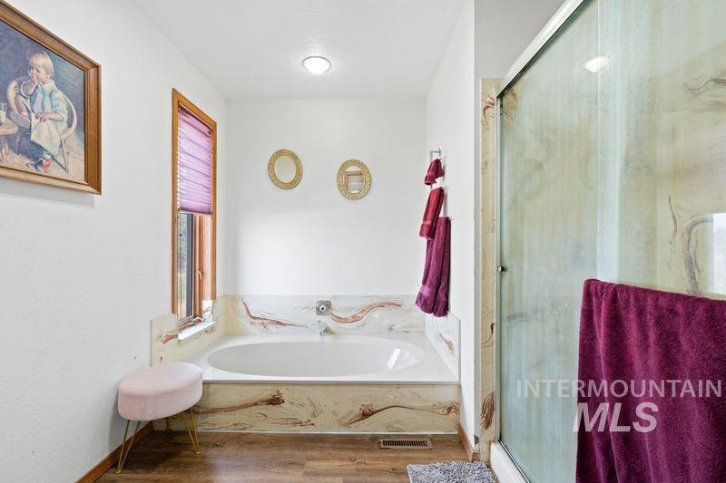 Bathroom featuring a garden tub, a shower stall, and wood finished floors