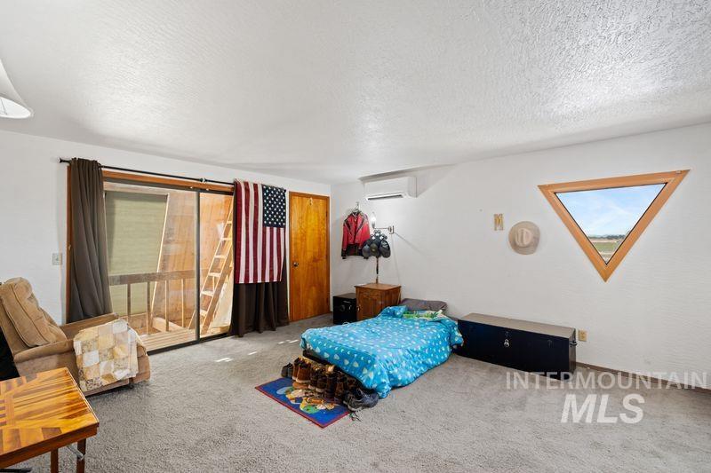 Carpeted bedroom with a textured ceiling, access to exterior, and a wall unit AC