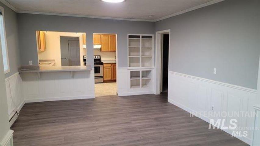 Unfurnished living room featuring ornamental molding, dark wood-style flooring, wainscoting, and a decorative wall