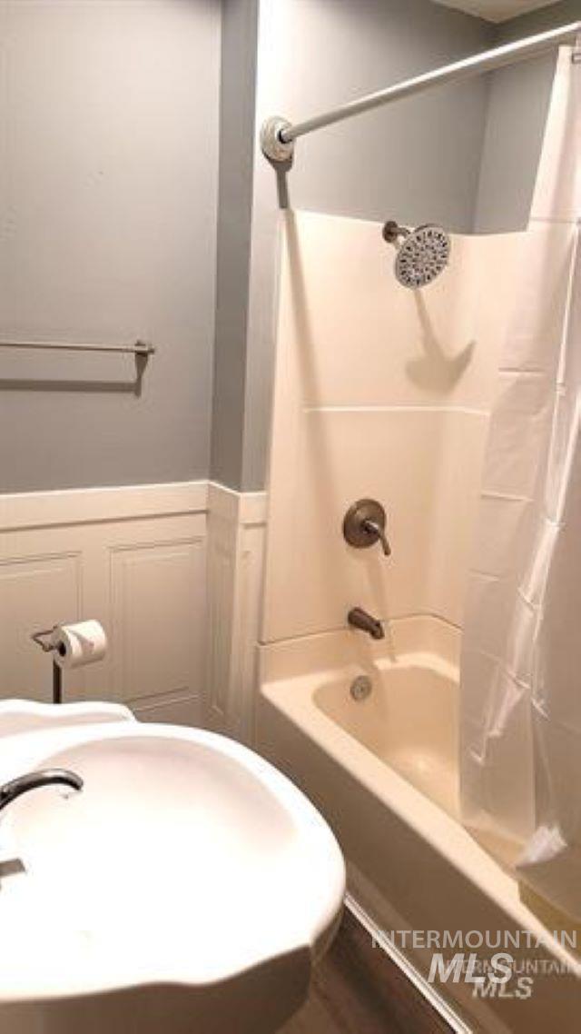 Bathroom featuring shower / bathtub combination with curtain and a wainscoted wall