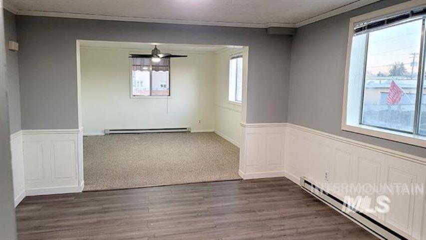 Unfurnished dining area with wainscoting, a baseboard radiator, a decorative wall, ornamental molding, and wood finished floors
