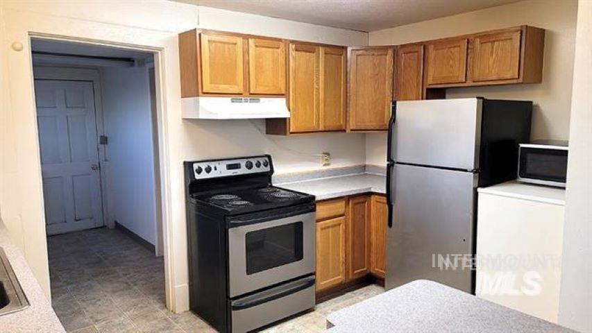 Kitchen with appliances with stainless steel finishes, light countertops, brown cabinets, and under cabinet range hood