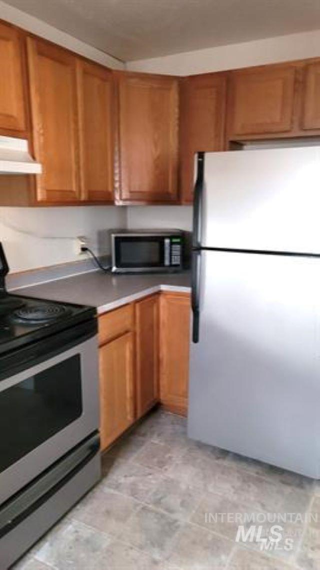 Kitchen with appliances with stainless steel finishes, brown cabinets, and range hood