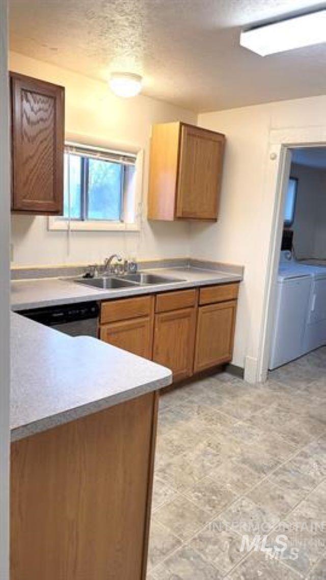 Kitchen with a textured ceiling, light countertops, dishwasher, and washer and dryer