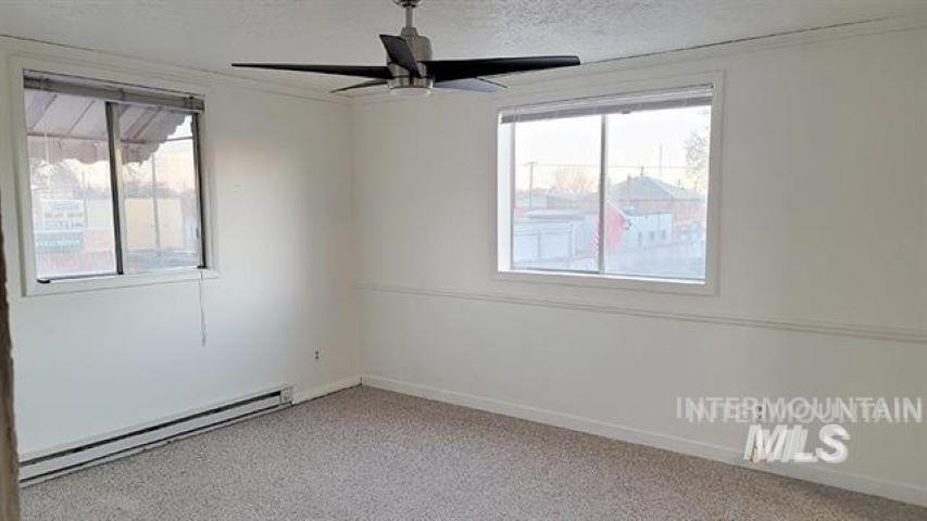 Empty room with baseboard heating, carpet flooring, a textured ceiling, ceiling fan, and crown molding