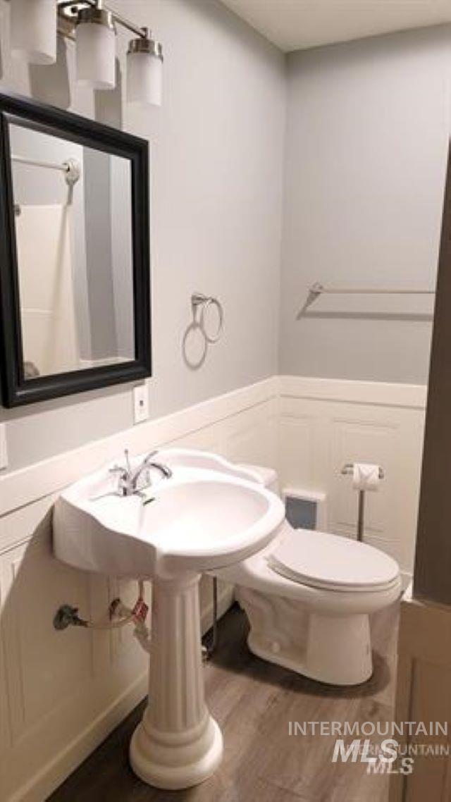 Half bath with wood finished floors, a wainscoted wall, and a decorative wall